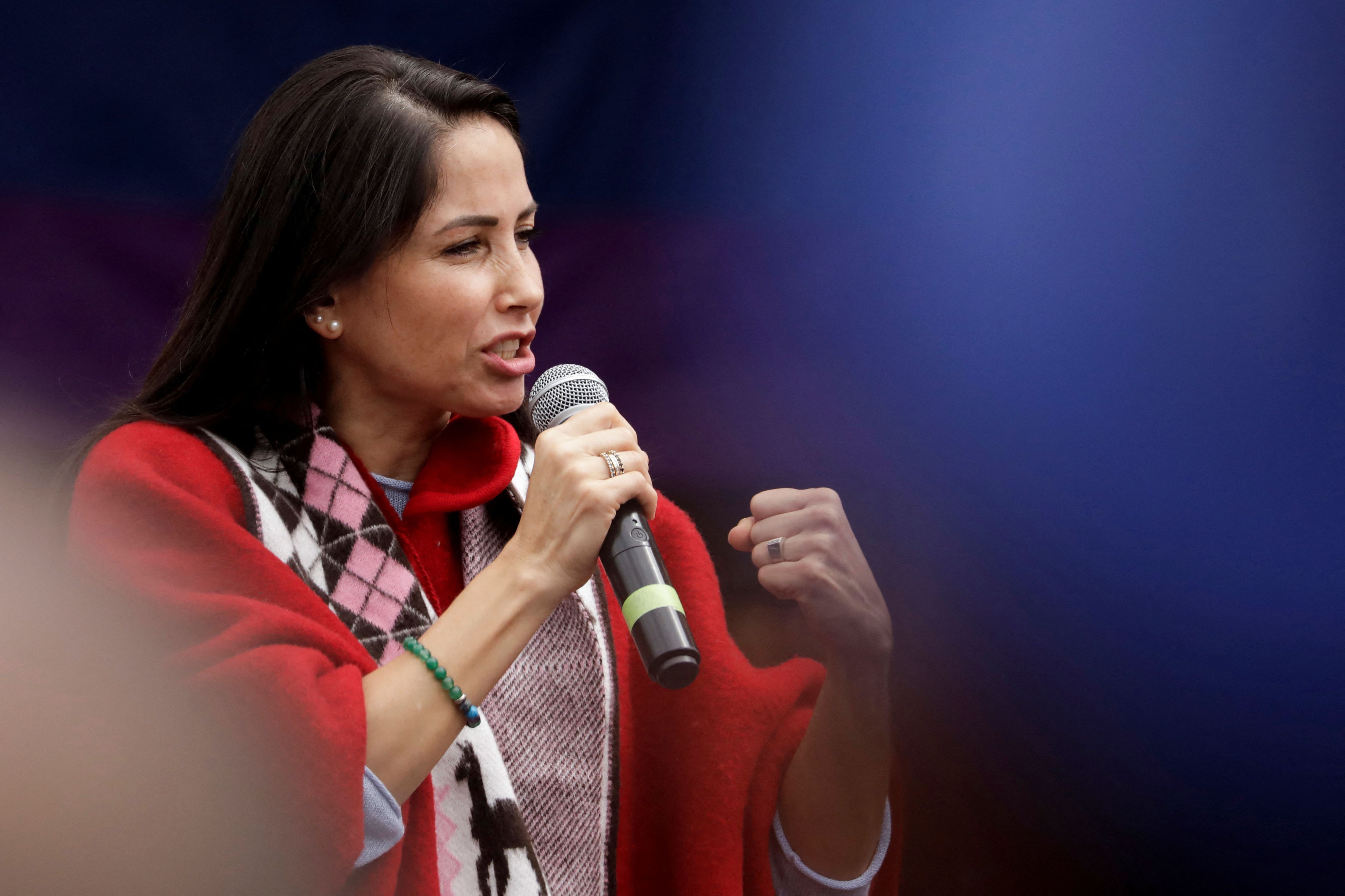 Luisa Gonzalez in Indigenous garb speaks into a microphone, with a fist gesturing in passion.