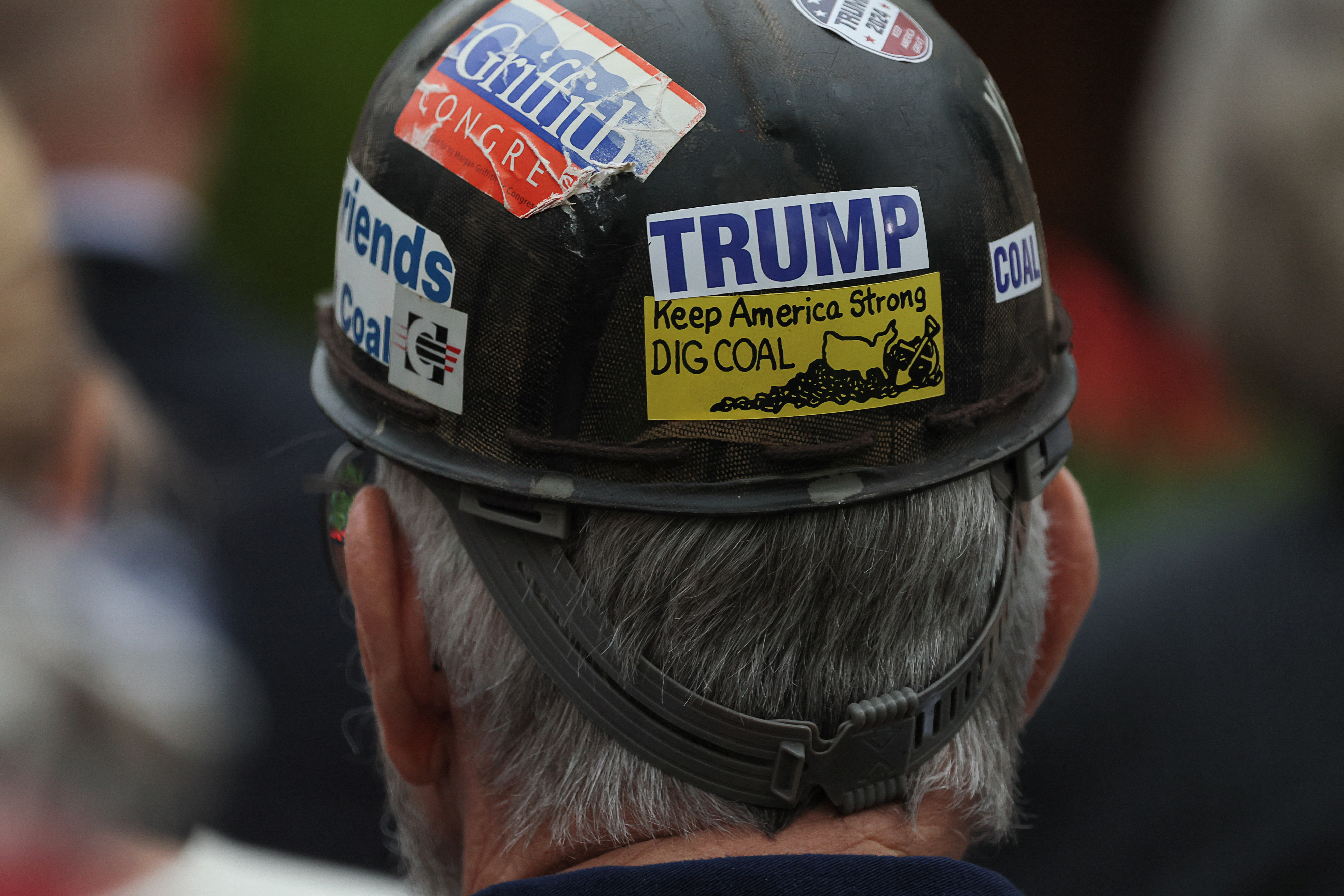 An audience member wears a hard hat with pro-Trump stickers