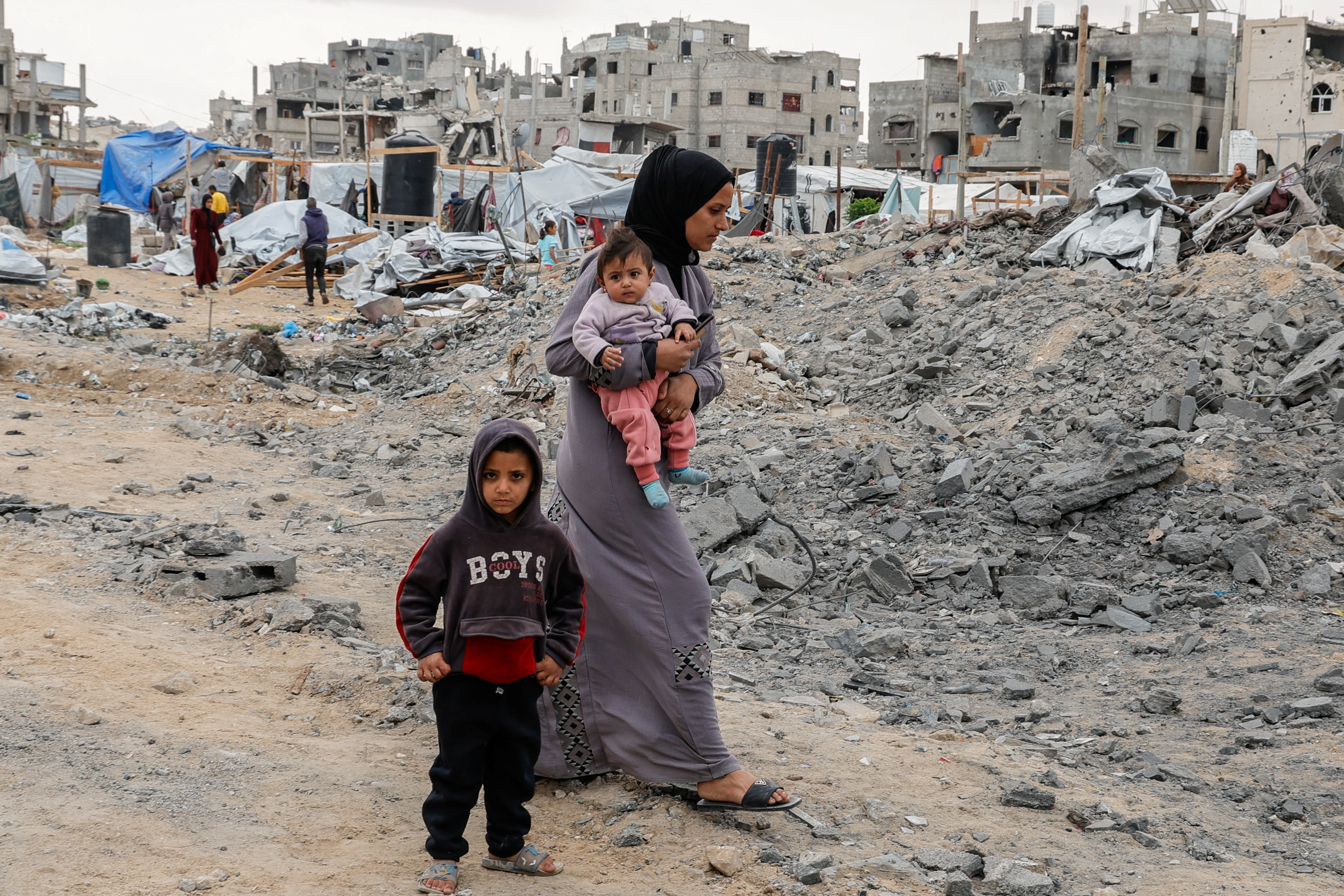 Woman, holding a child, walks past the rubble in Gaza