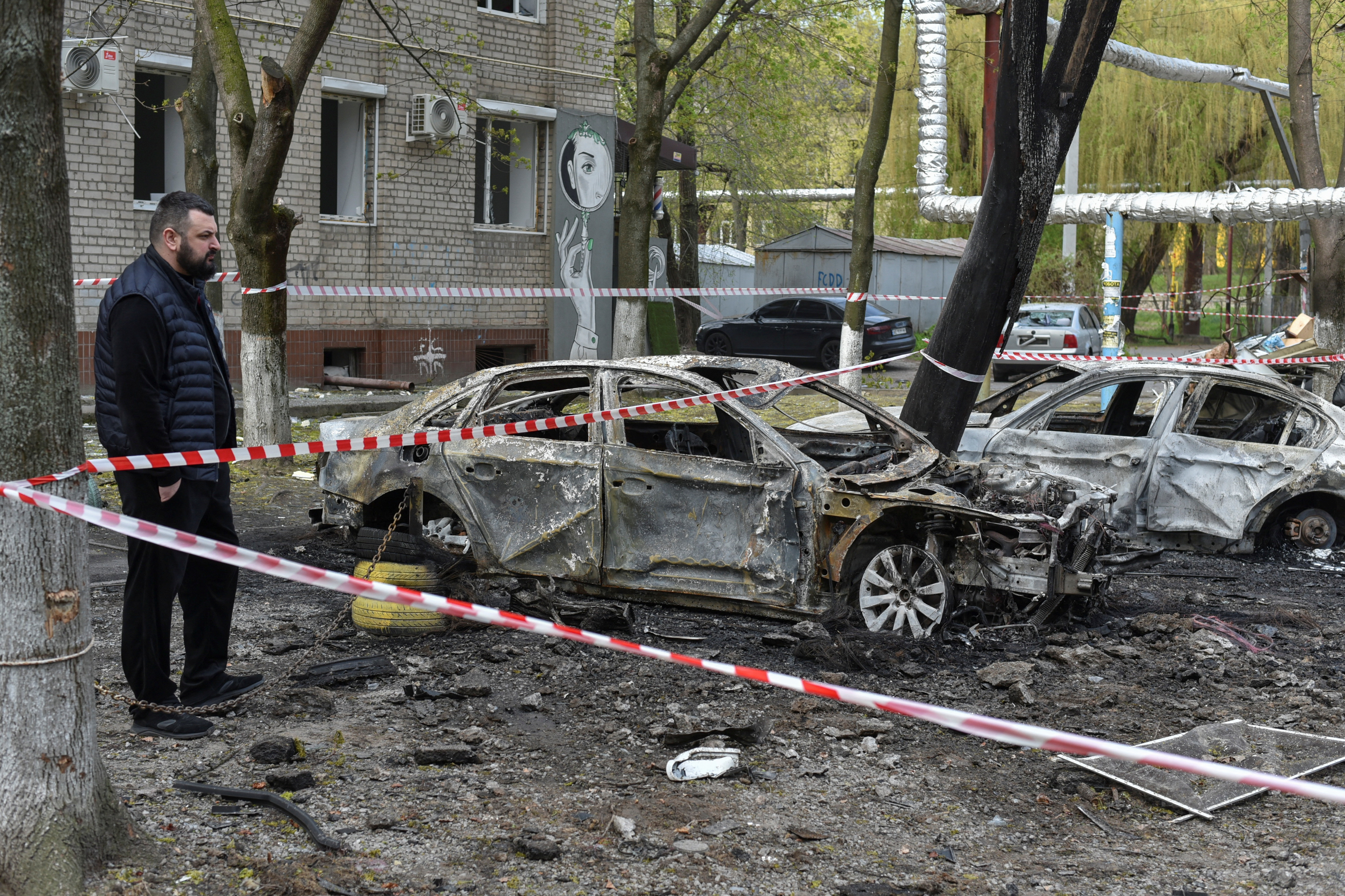 A resident stands next to burned cars at the site of a Russian drone attack.