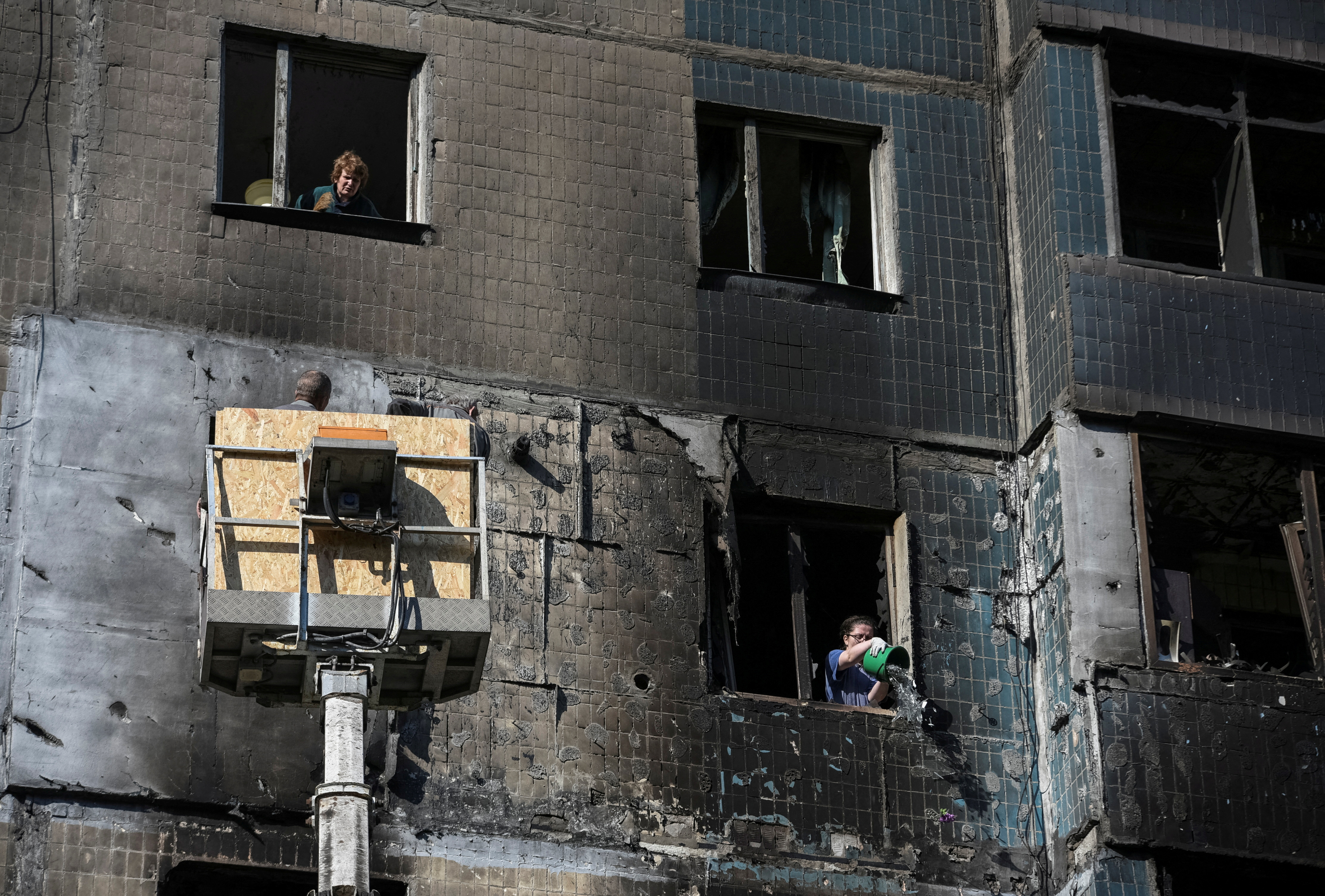 A woman speaks with workers covering broken windows as her neighbor throws debris out of her flat window in an apartment building which was damaged by a Russian drone strike, amid Russia's attack on Ukraine, in the town of Kamyanske in Dnipropetrovsk region, Ukraine April 26, 2025. REUTERS/Mykola Synelnykov TPX IMAGES OF THE DAY