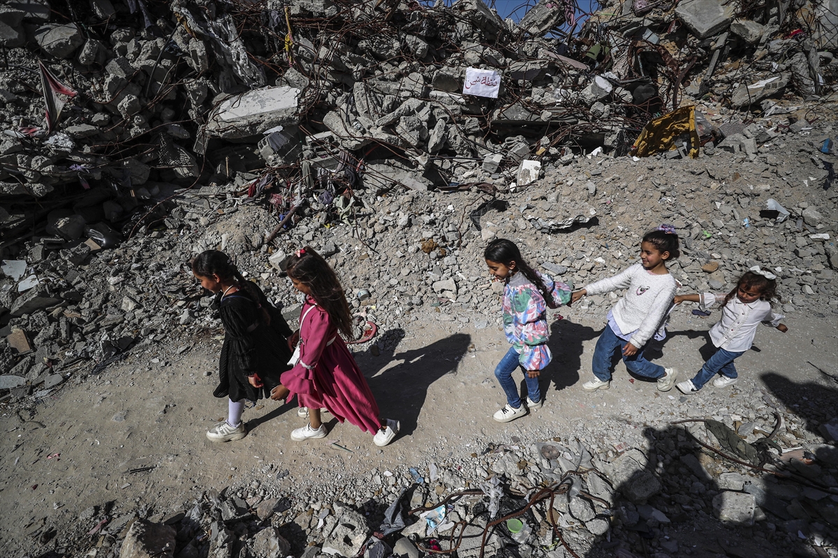 children hold hands as they walk between the rubble of destroyed buildings wearing nice clothes