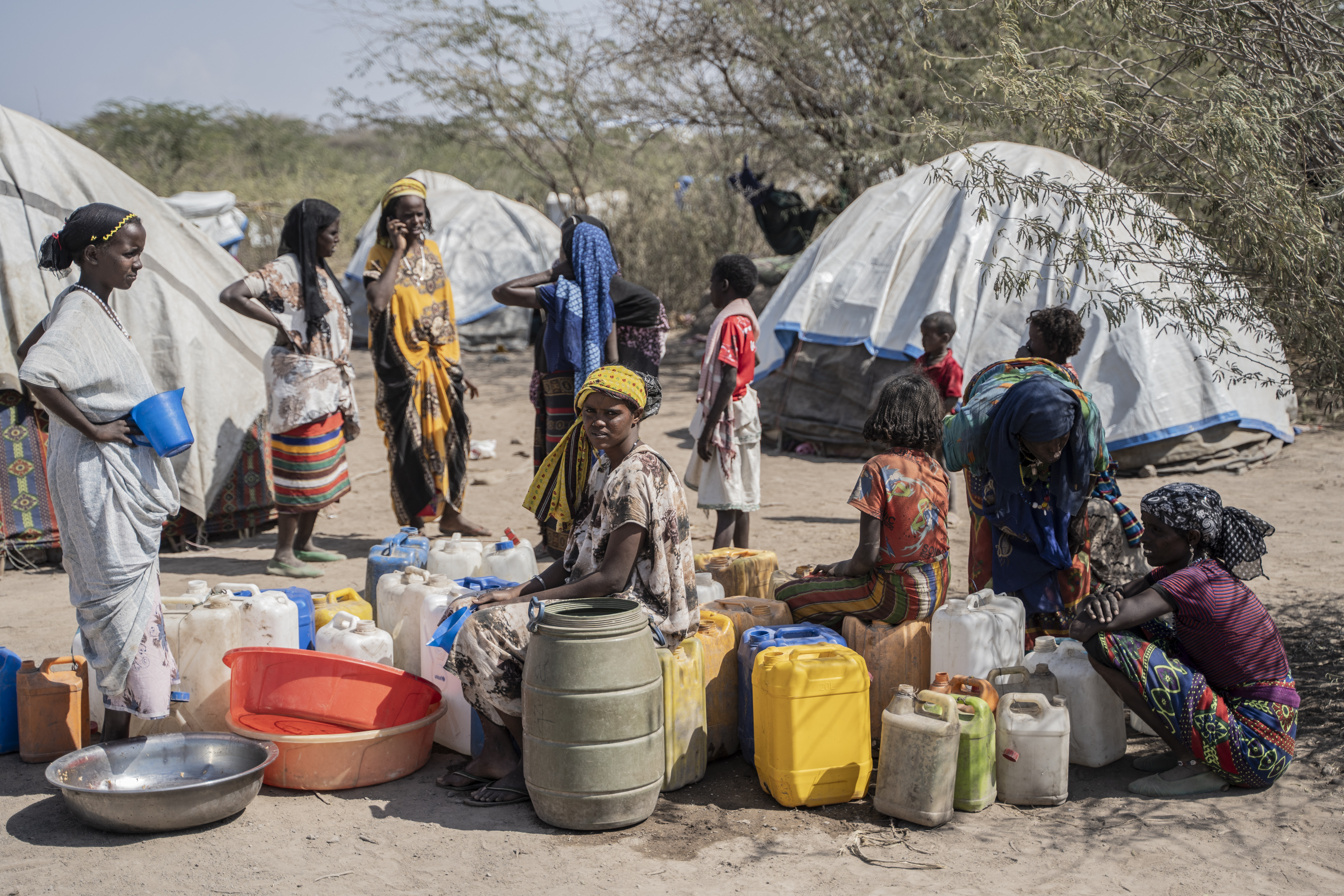 Displaced people wait in line to fill their jars at a water point in a displacement camp.
