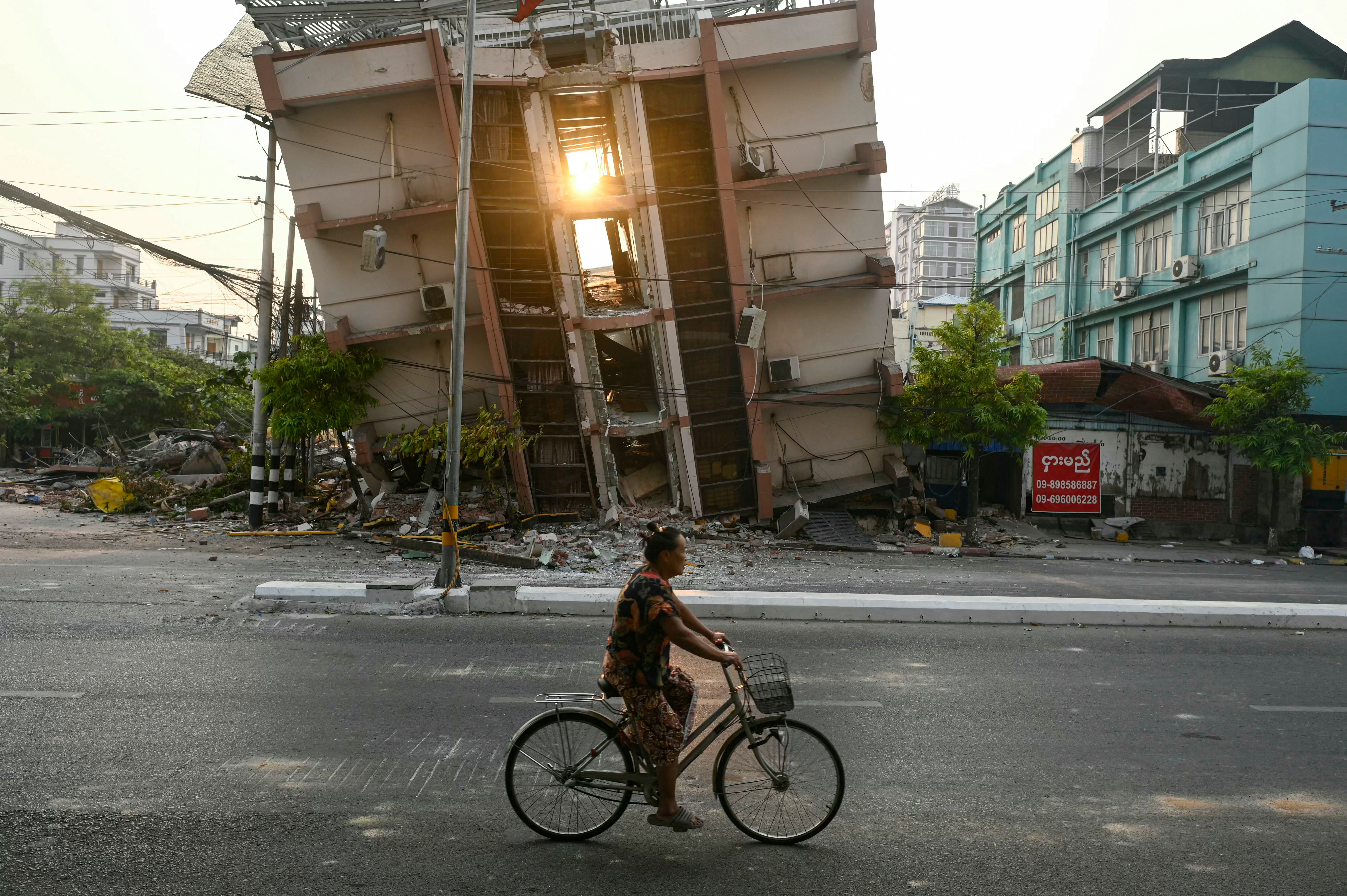 A woman rides her bicycle past a collapsed building in Mandalay