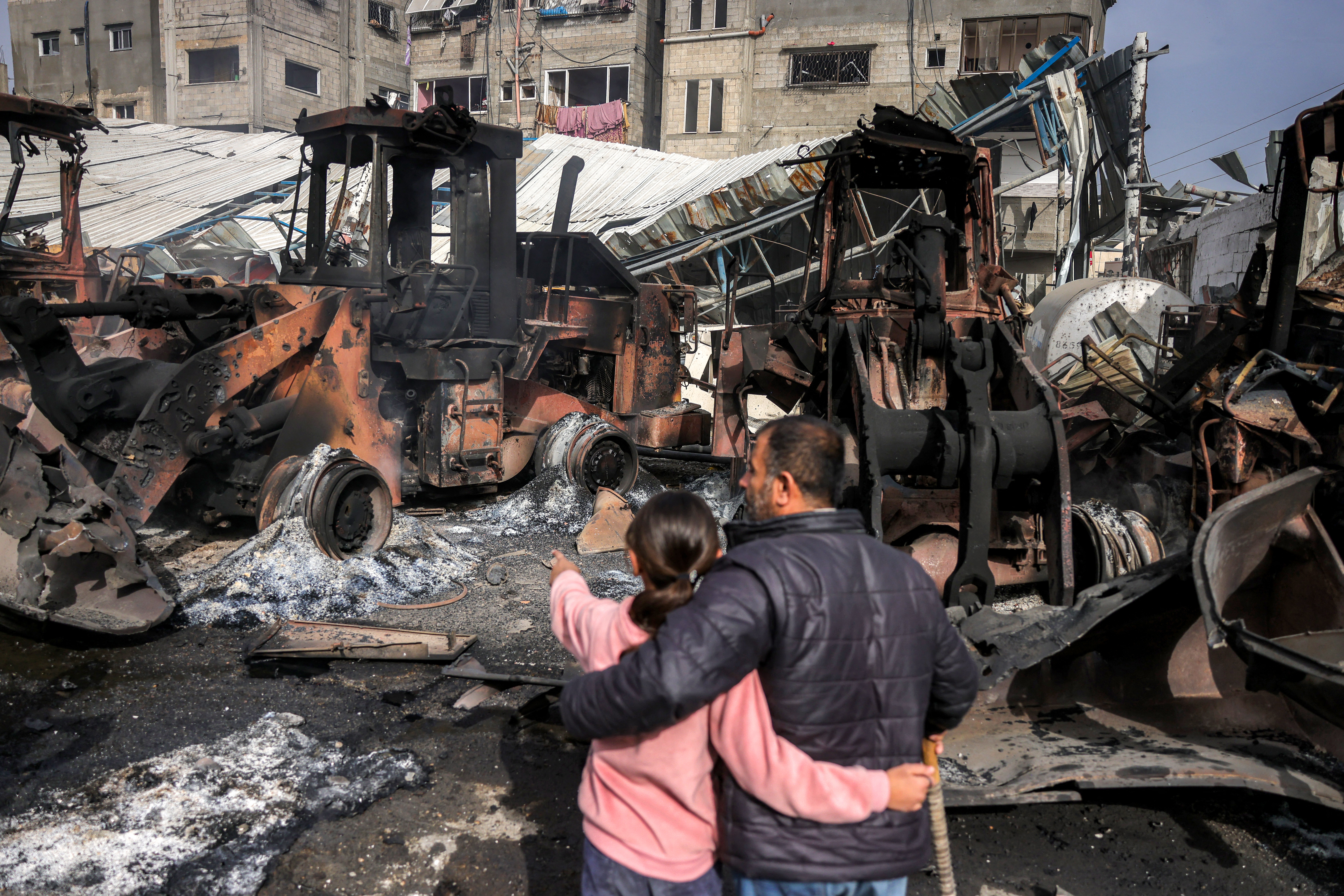 A girls stands embracing a man as they inspect destroyed bulldozers
