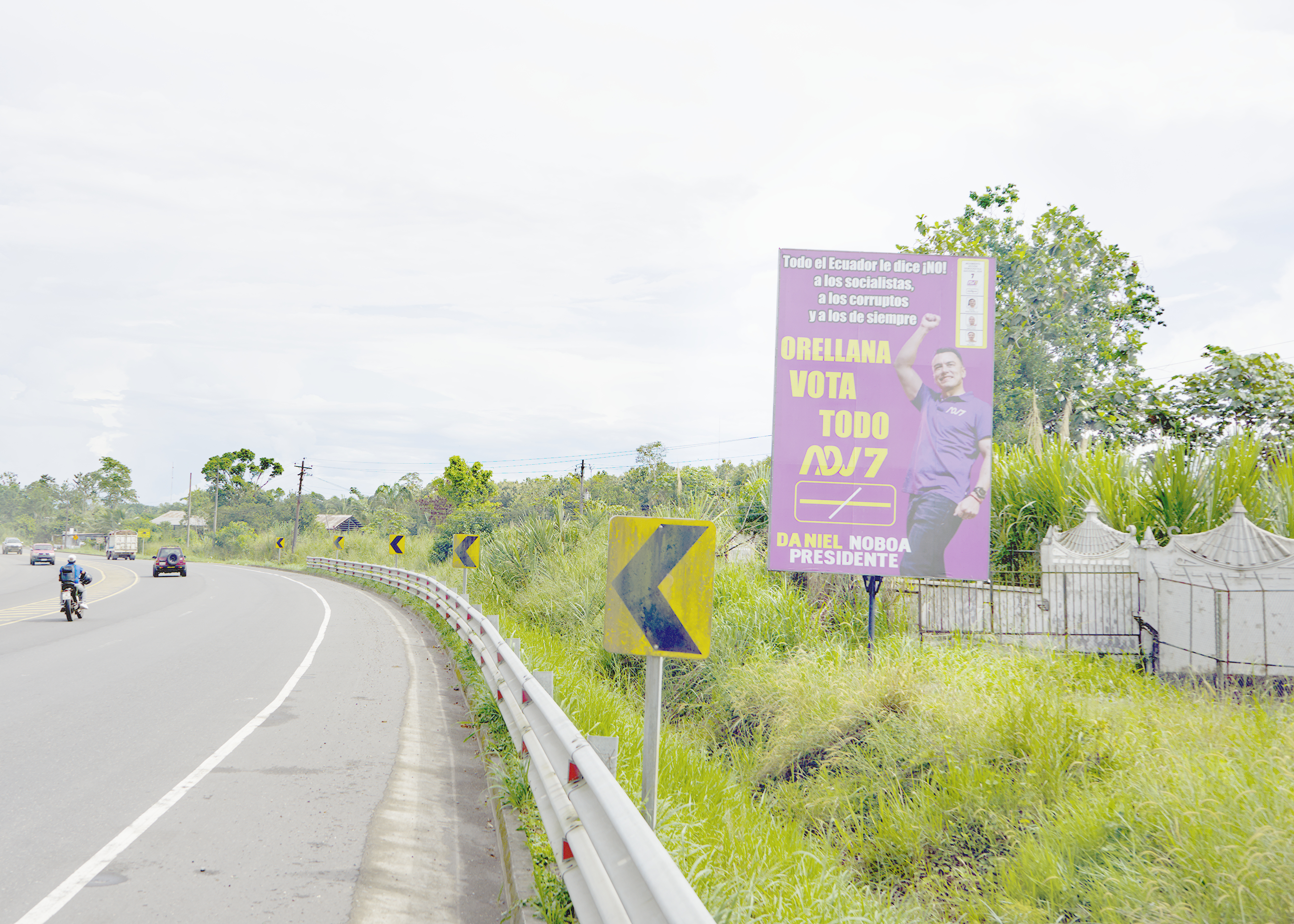 A roadside sign in Ecuador advertises the re-election campaign of Daniel Noboa. It is a pop of purple against a grassy green landscape in Orellanas, Ecuador.