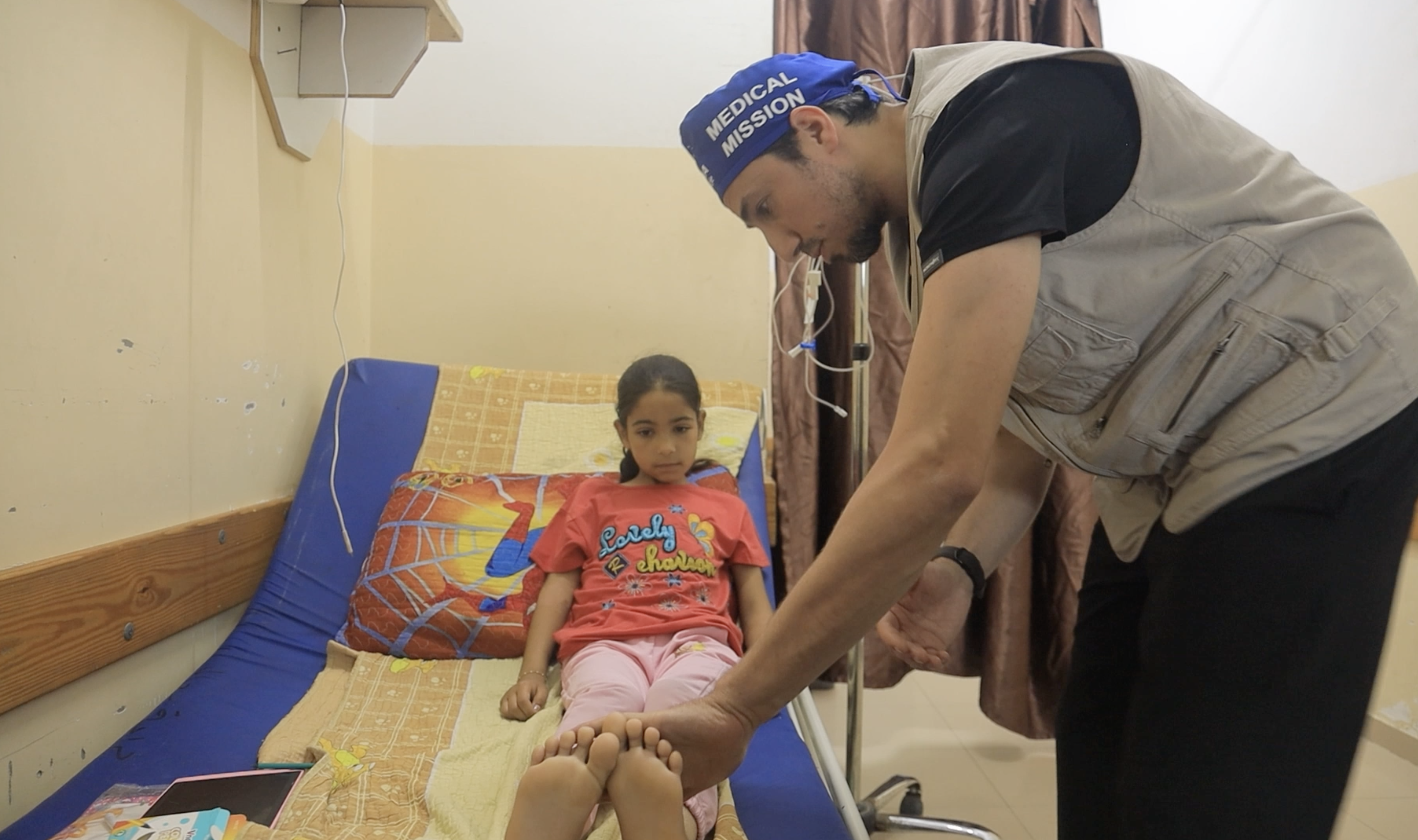 A doctor leans over a little girl, moving her leg to check healing