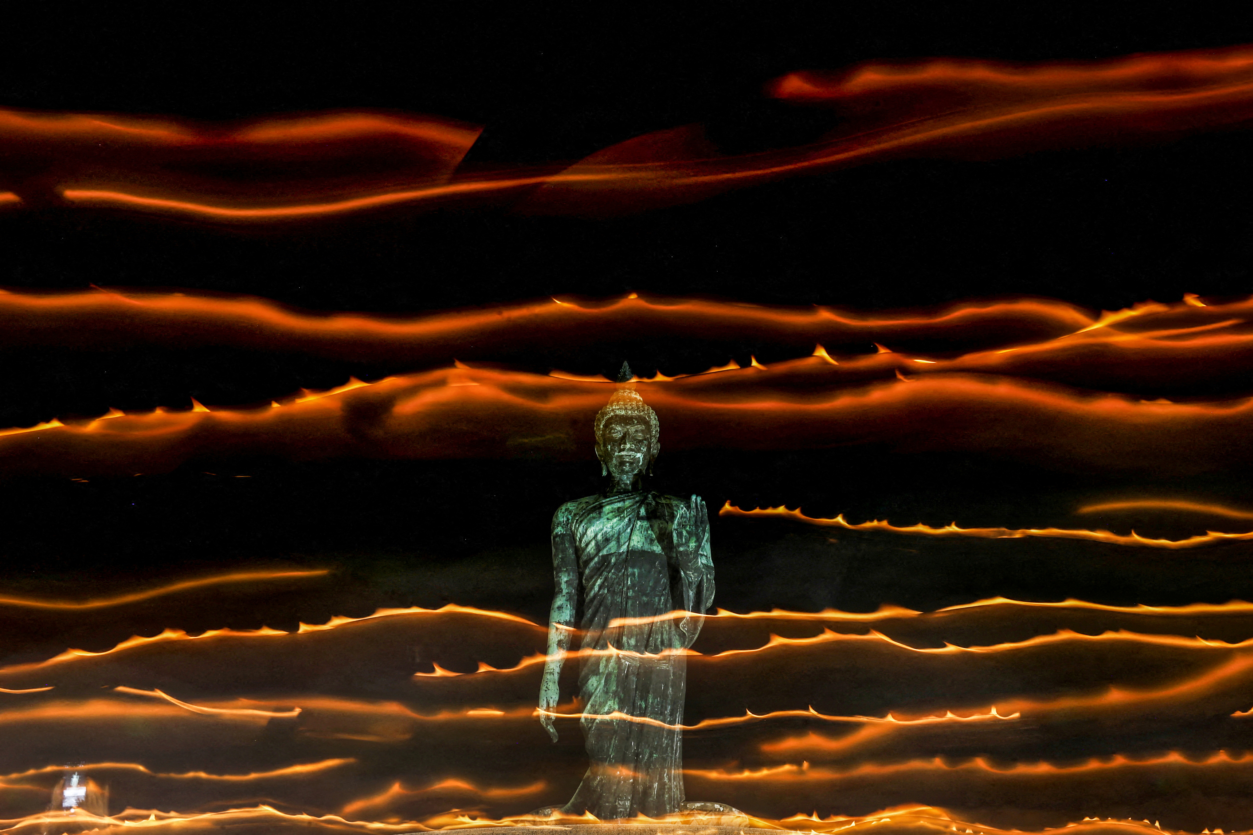 People walk with candle lights around a large Buddha statue during a ceremony commemorating Asalha Puja Day, an annual celebration marking the beginning of Triple Gem at a temple in Nakhon Pathom province on the outskirts of Bangkok, Thailand [File: Chalinee Thirasupa/Reuters]