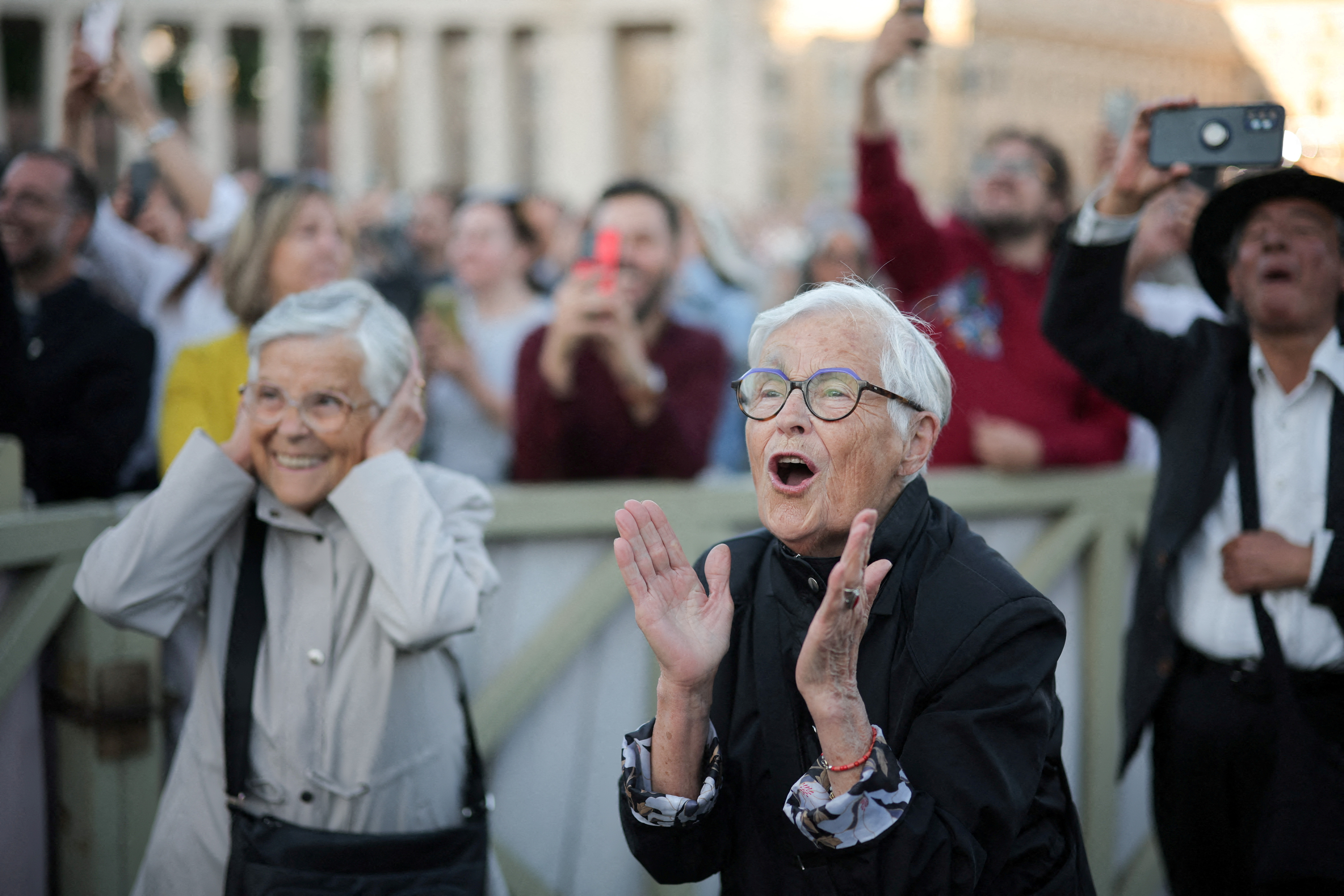 Two elder women clap and hoot — one shielding her ears from the noise — as a new pope is announced at the Vatican
