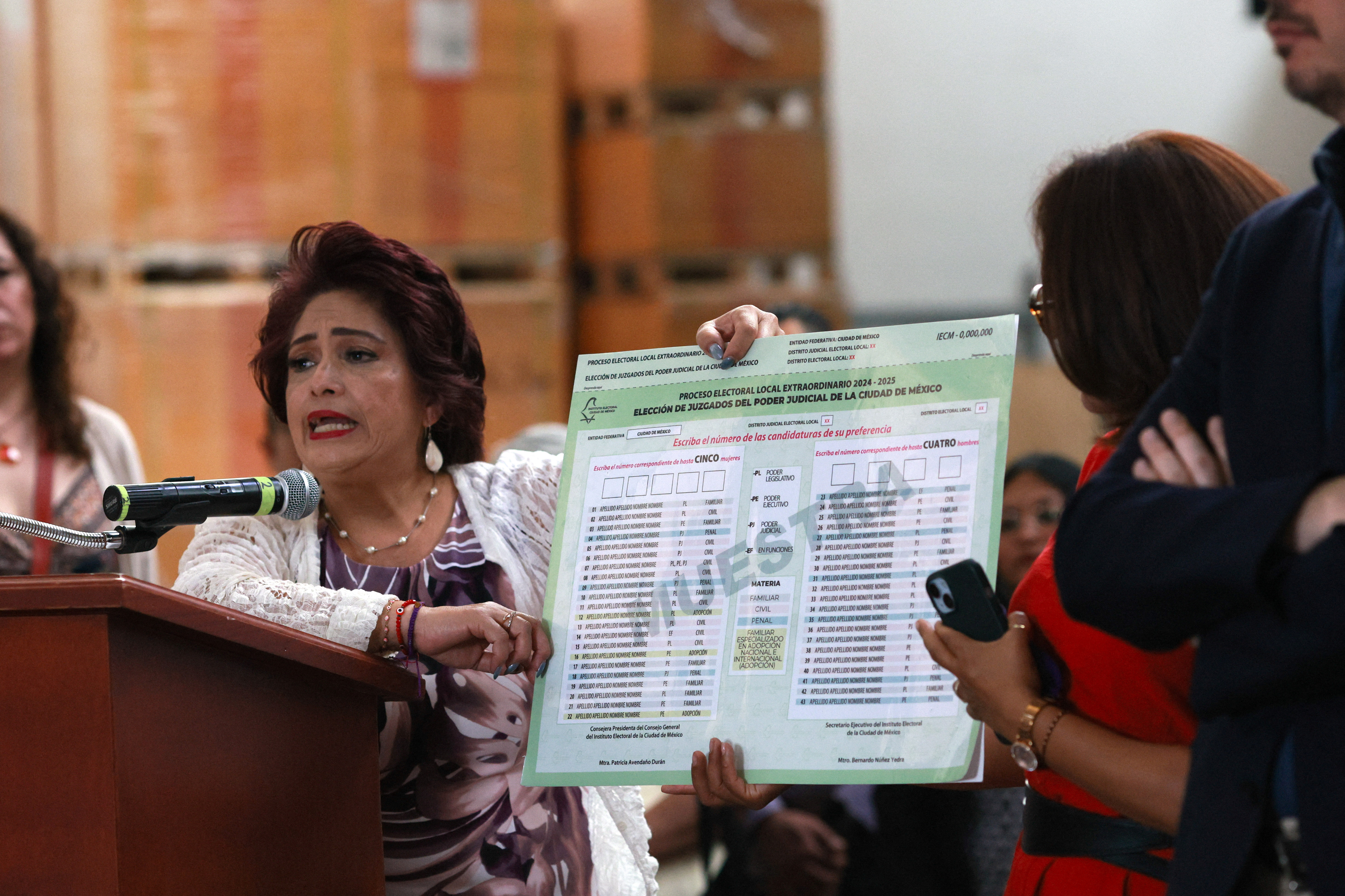 Electoral official Patricia Avendano holds up a sample ballot that is protected in a plastic cover.