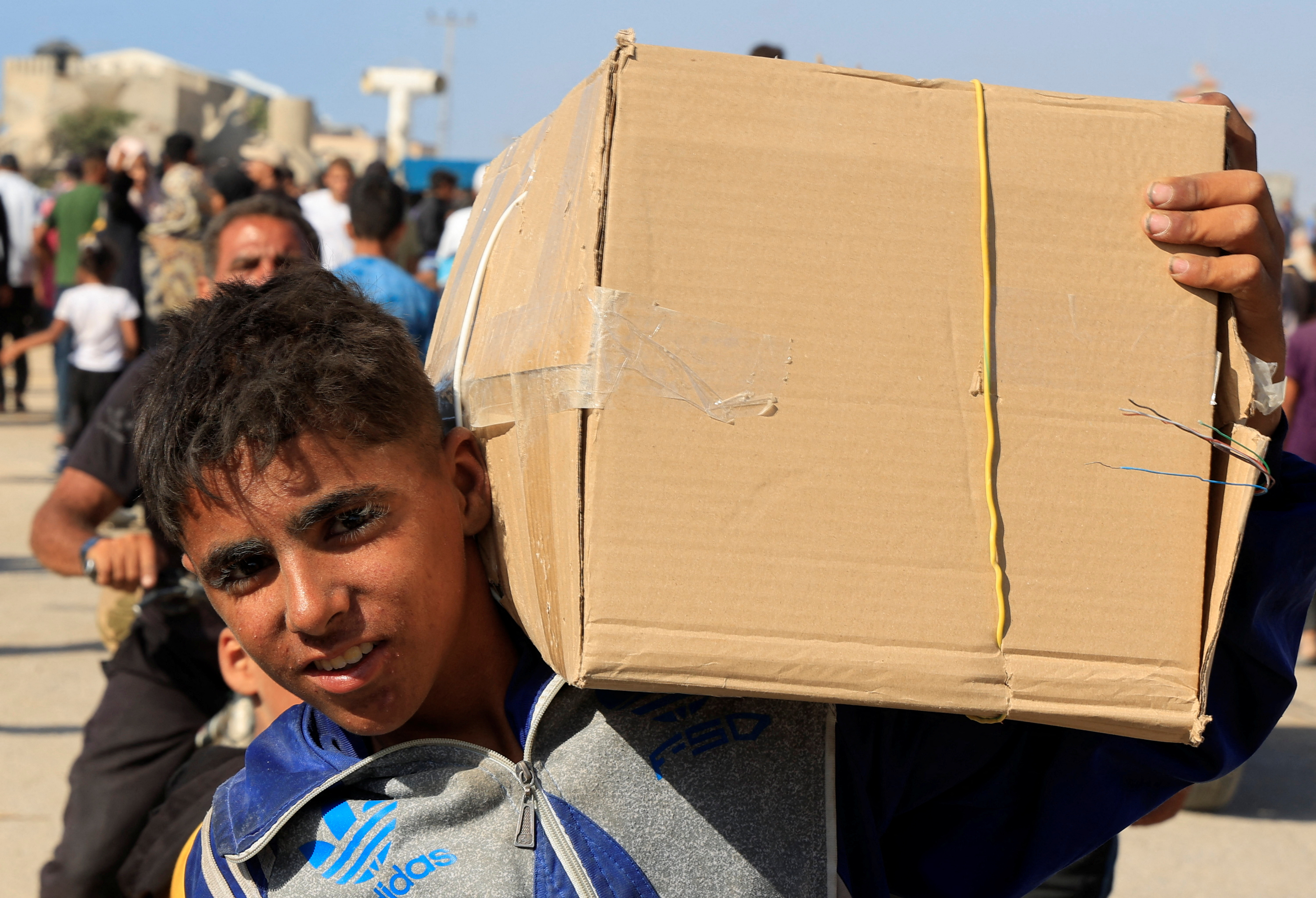 A young boy carries a bulging cardboard box on his shoulder