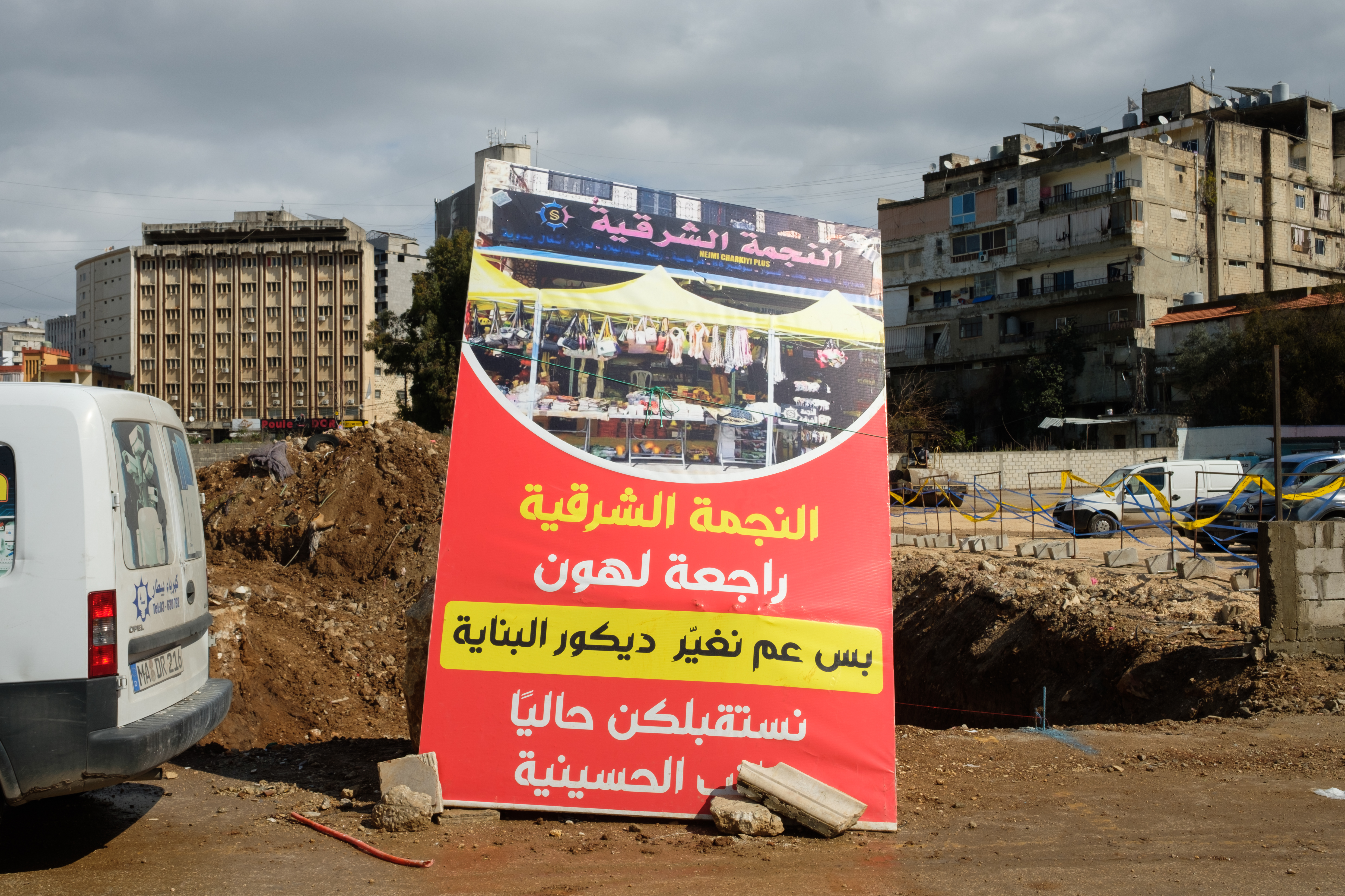 A red sign is propped up in front of a lot with piles of rubble and a huge hole