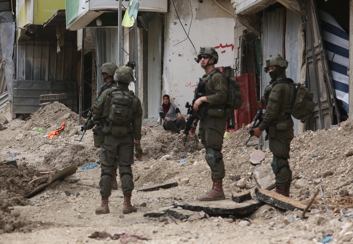 armed soldiers stand in front of a woman sitting on the ground on a dirt street