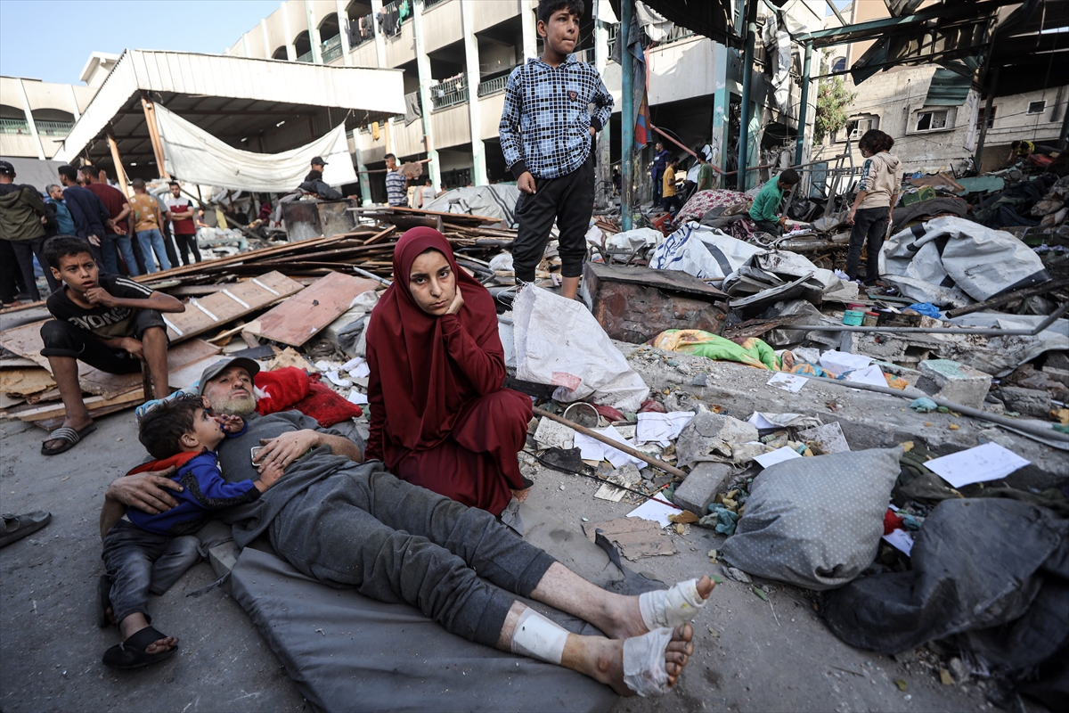 a family sit next to an injured man in front of destroyed buildings