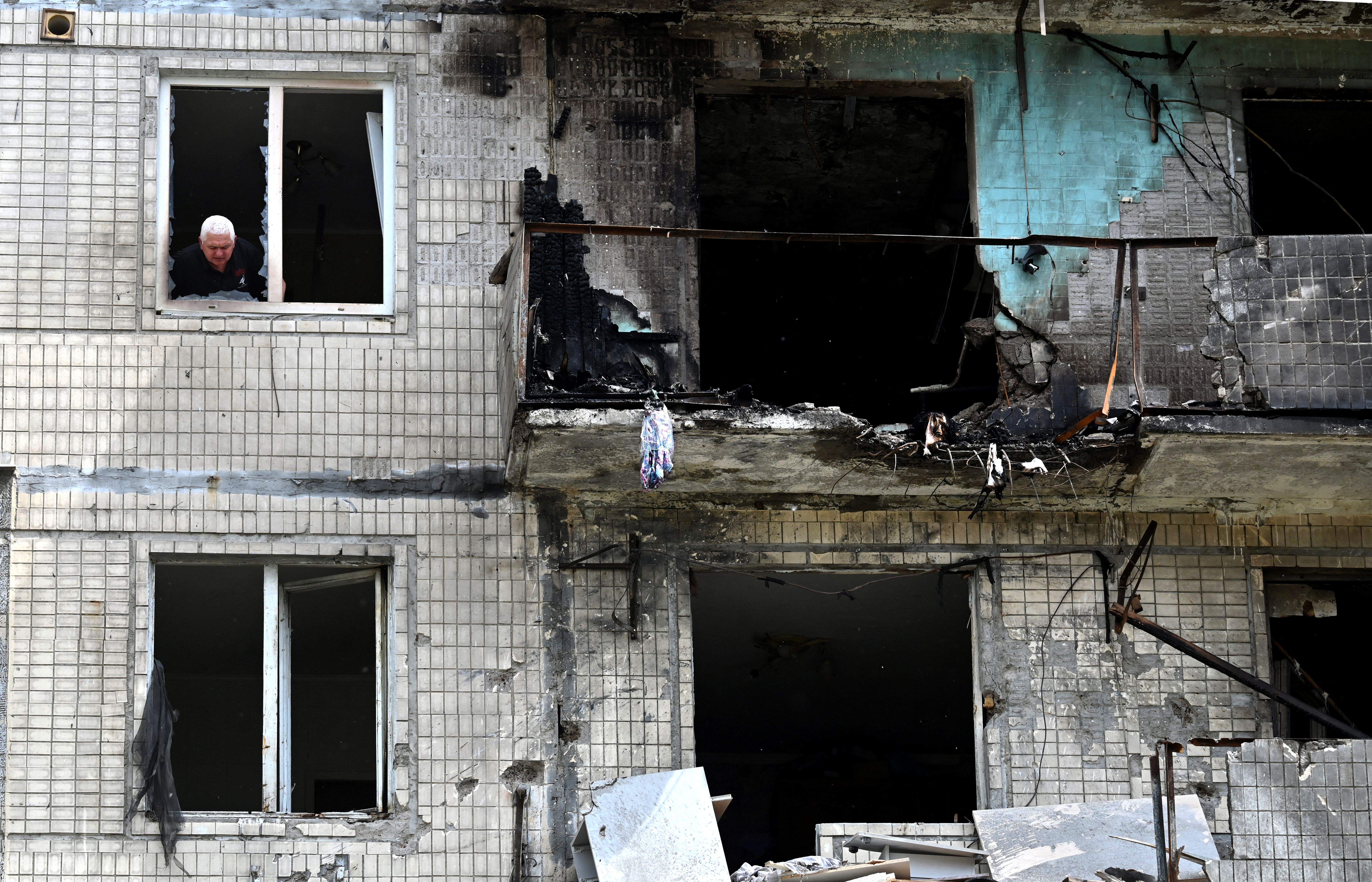 A local resident looks out of the window of his flat in a damaged, multistorey residential building.