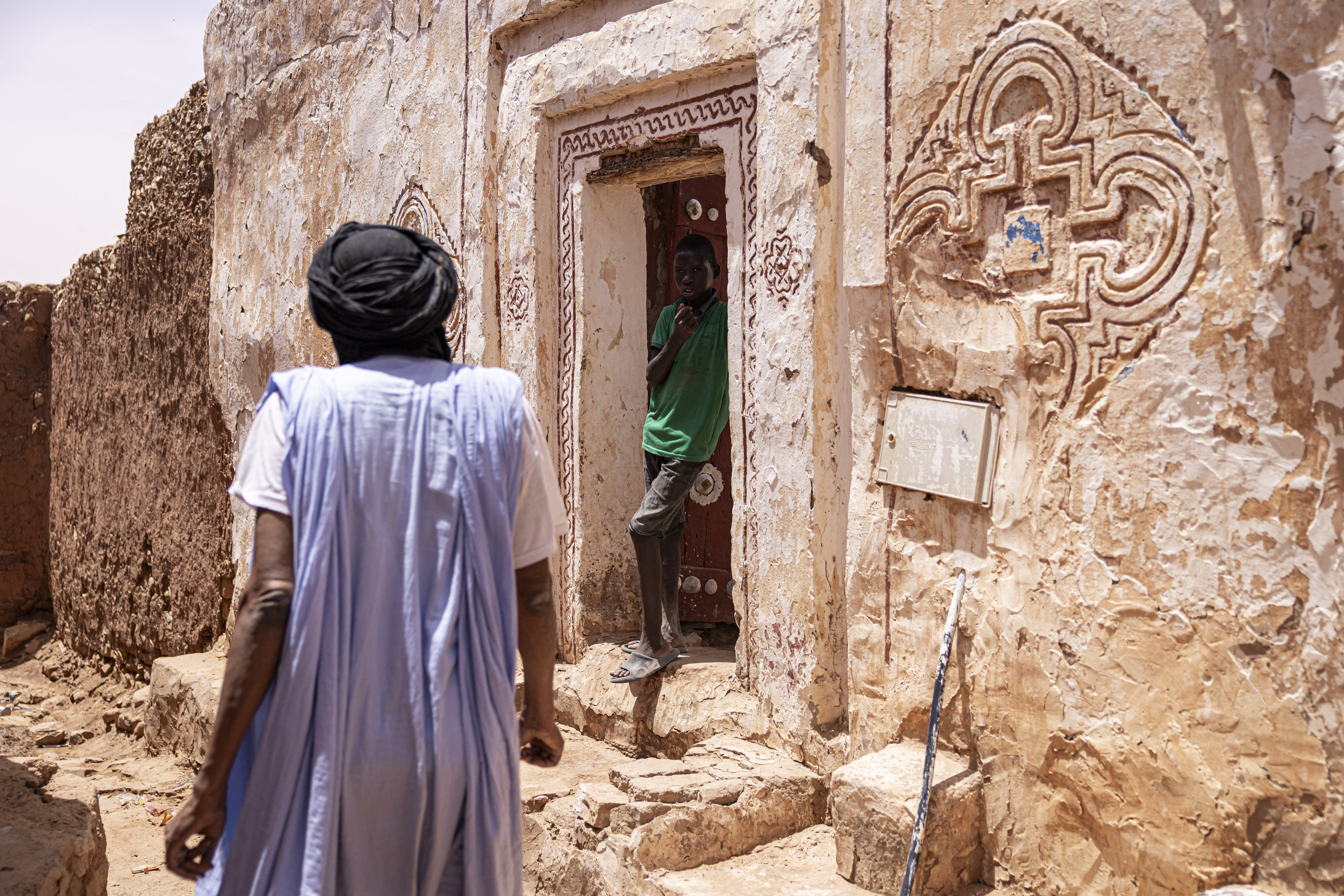 A boy stands outside a house decorated with traditional paintings in the old town section of Oualata