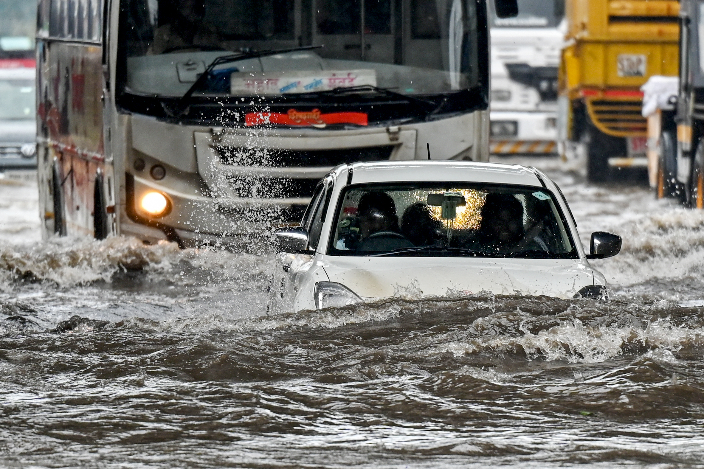 A car lies partially submerged as it wades through a flooded street.