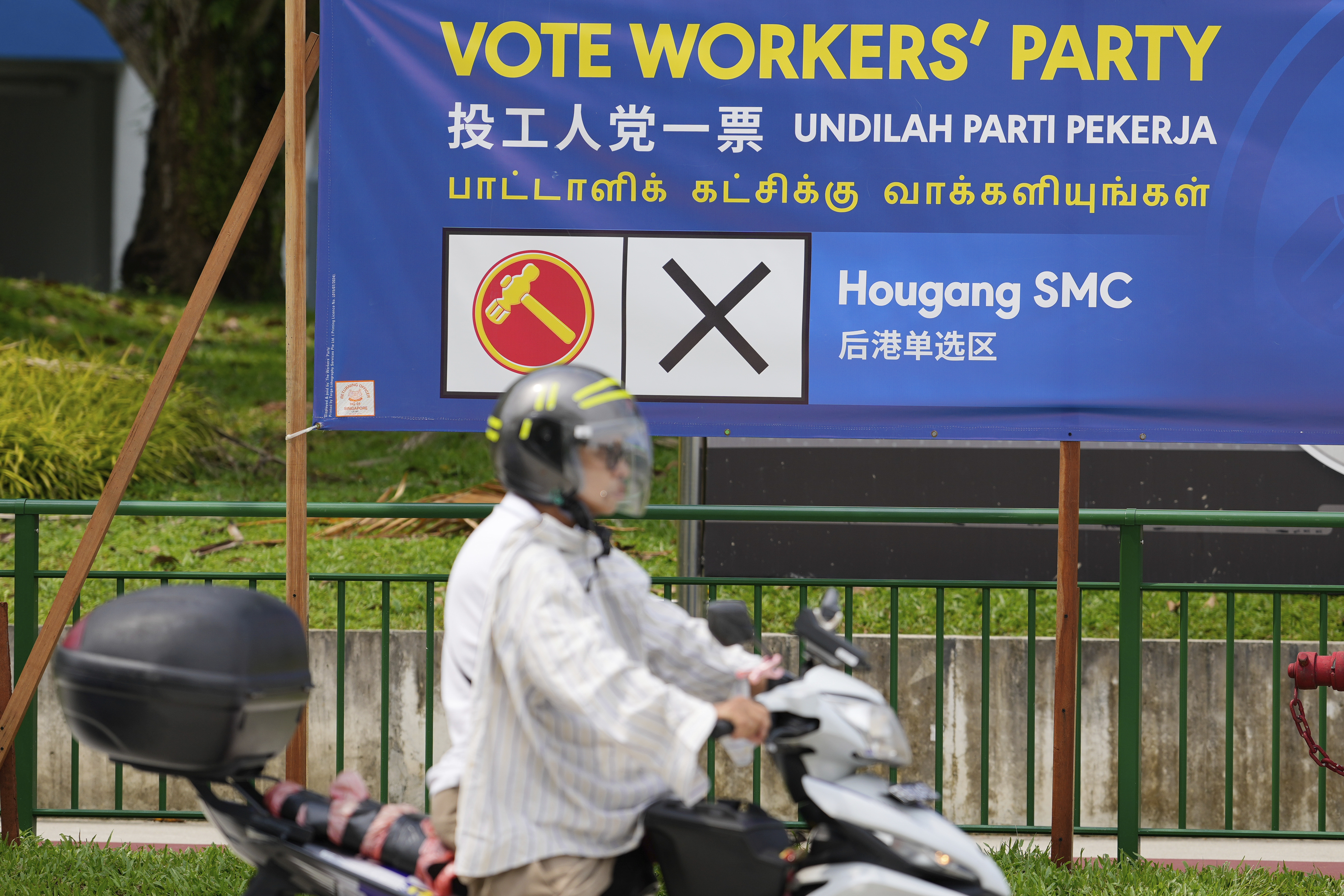 A Singaporean rides his motorcycle pass a workers' party board at Hougang area in Singapore, Friday, May 2, 2025. (AP Photo/Vincent Thian
