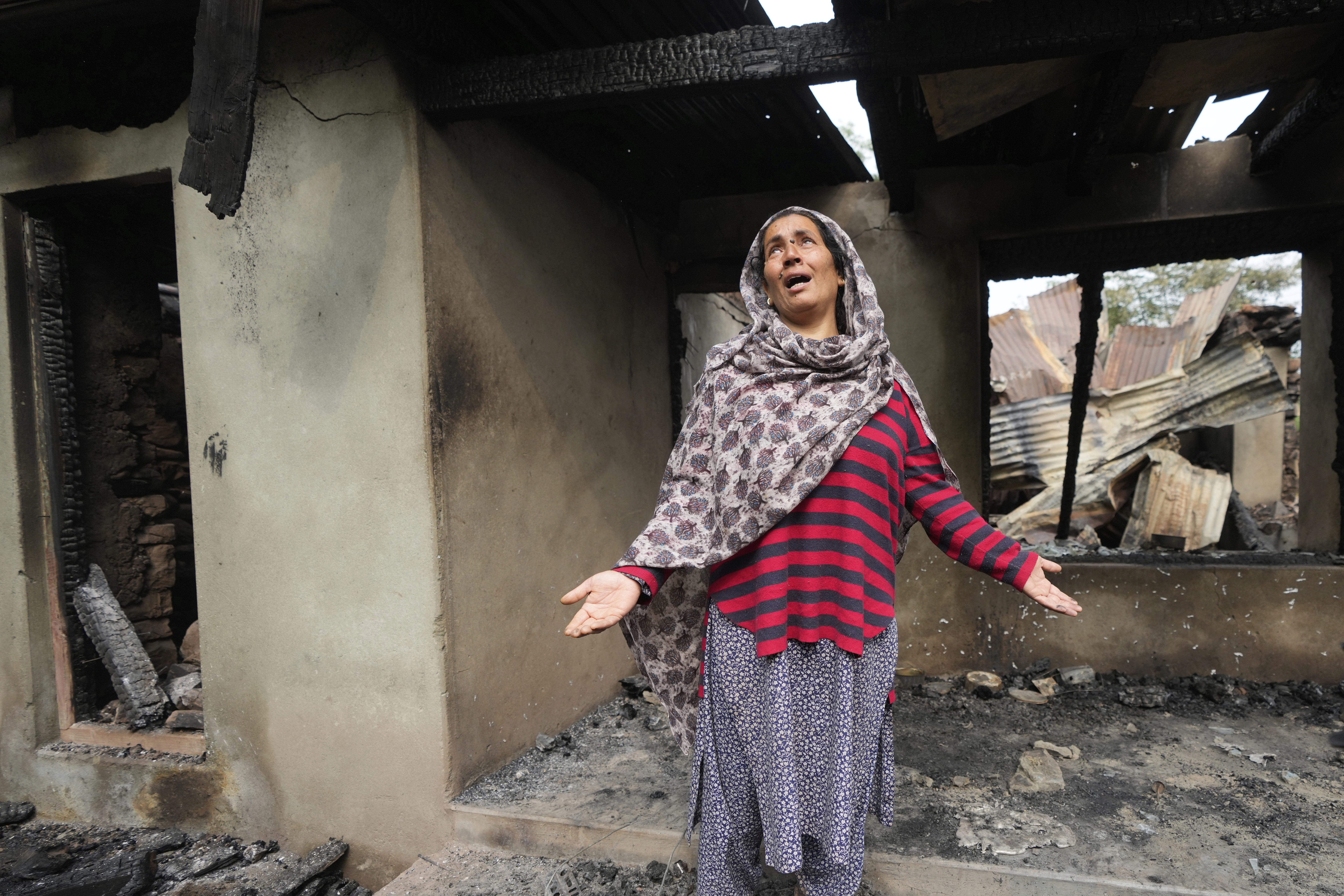 Rubina Begum wails as she stands outside her house damaged by Pakistani artillery shelling