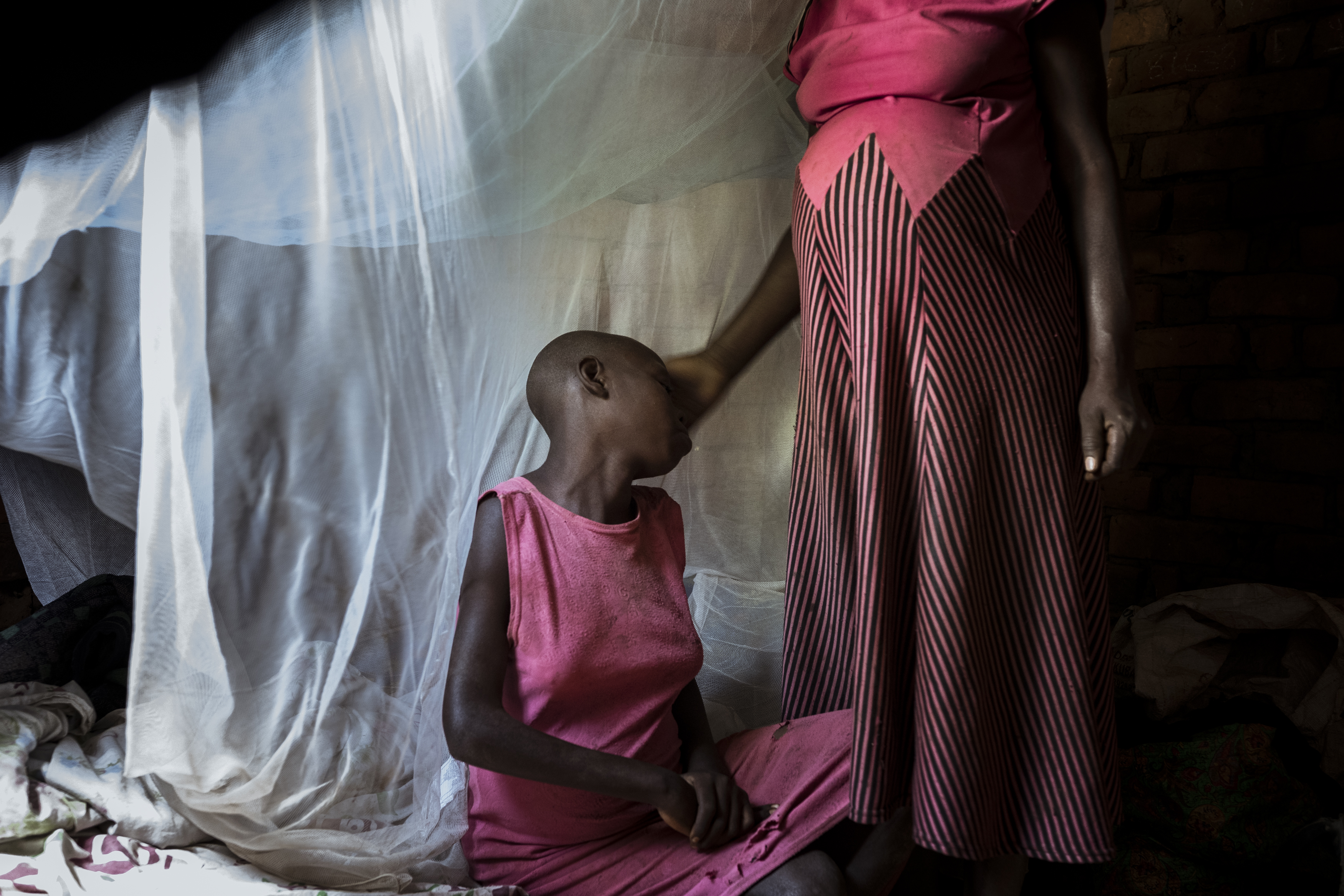 Busede, Uganda. 13-year-old Janet Akwatulira is comforted by her mother Florence Nakecho in the bedroom they share with Janet's sister Jimbo. Janet and Jimbo both live with undiagnosed intellectual disabilities. Janet is currently seven months pregnant because of rape. The family know the attacker, a 37-year-old neighbour, who has fled the area. The family of the alleged rapist offered Florence a bar of soap and a bag of sugar each month until the baby is born as compensation. Florence agreed but the deal was then reneged. As a result, Florence went to the local police who informed her that if she continued to press charges against the rapist, she herself would be arrested on grounds of neglect. While the health system in Uganda is flawed towards people living with disability, the justice system also plays a part in their community ostracization. Florence is a subsistent sugar cane worker who is also seven months pregnant. When the two babies are born, who will care for them and who will be able to earn a living is a question they have no answers for. [Christopher Hopkins/Al Jazeera]