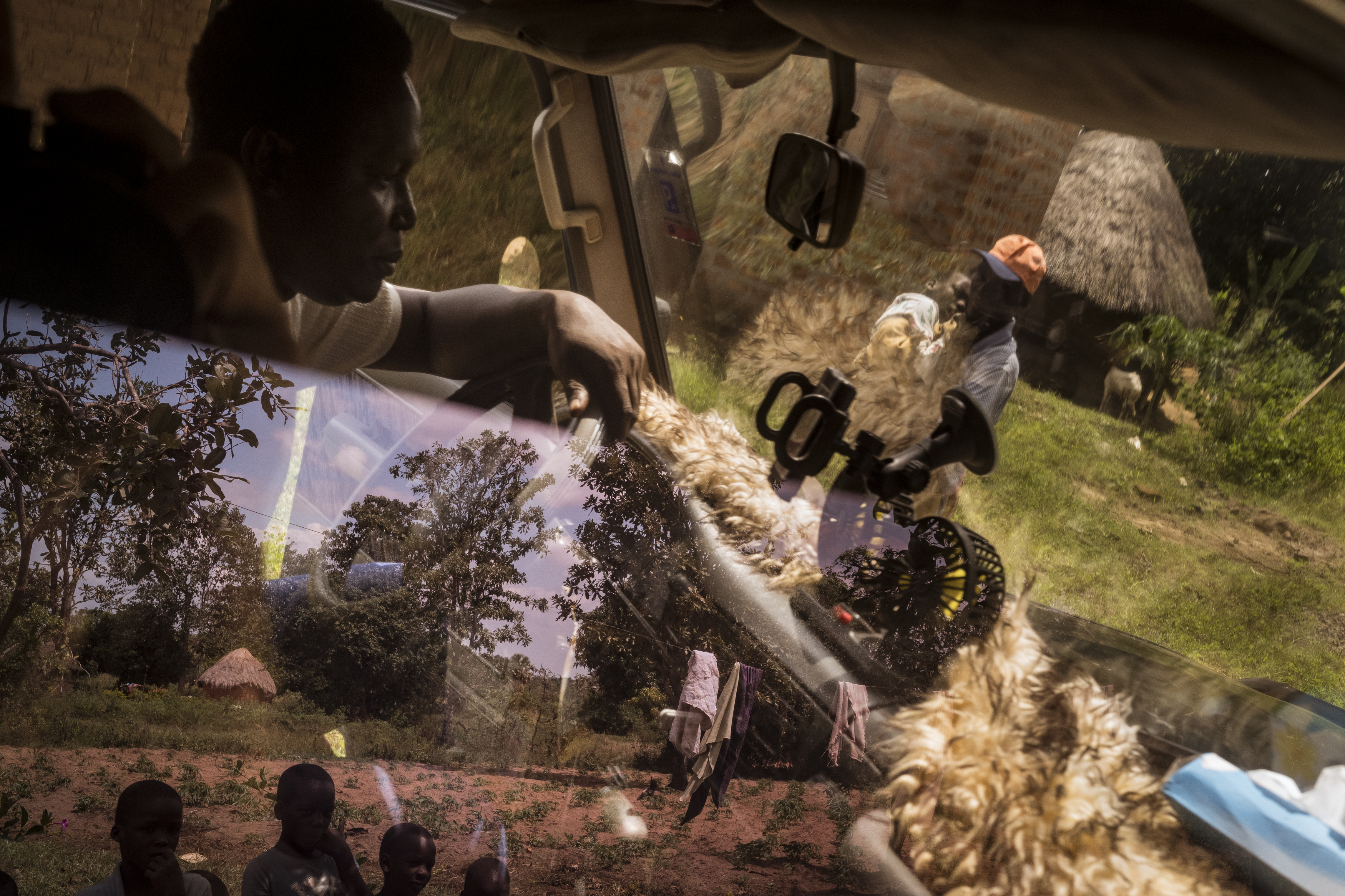 Oukot, Amuria District, Soroti. Local children watch on as Simon Okurut carries his son Paul Oribo, who lives with Cerebral Palsy, to the Landcruiser Fred Alimet from local charity Cherish Ikoku Uganda uses as a makeshift ambulance. Alimet has identified Uganda’s transport system as a major factor in families being unable to access proper healthcare. Roads are often un-usable, public transport is limited to major urban centres and there is no reliable ambulance service. The country has 178 Ambulances. It needs 460 to reach its goal of one per 100,000 people. Fred and CIU were able to raise $2500USD in donations to purchase a second-hand 4WD which they operate for families affected by disability as a surrogate ambulance. [Christopher Hopkins/Al Jazeera]