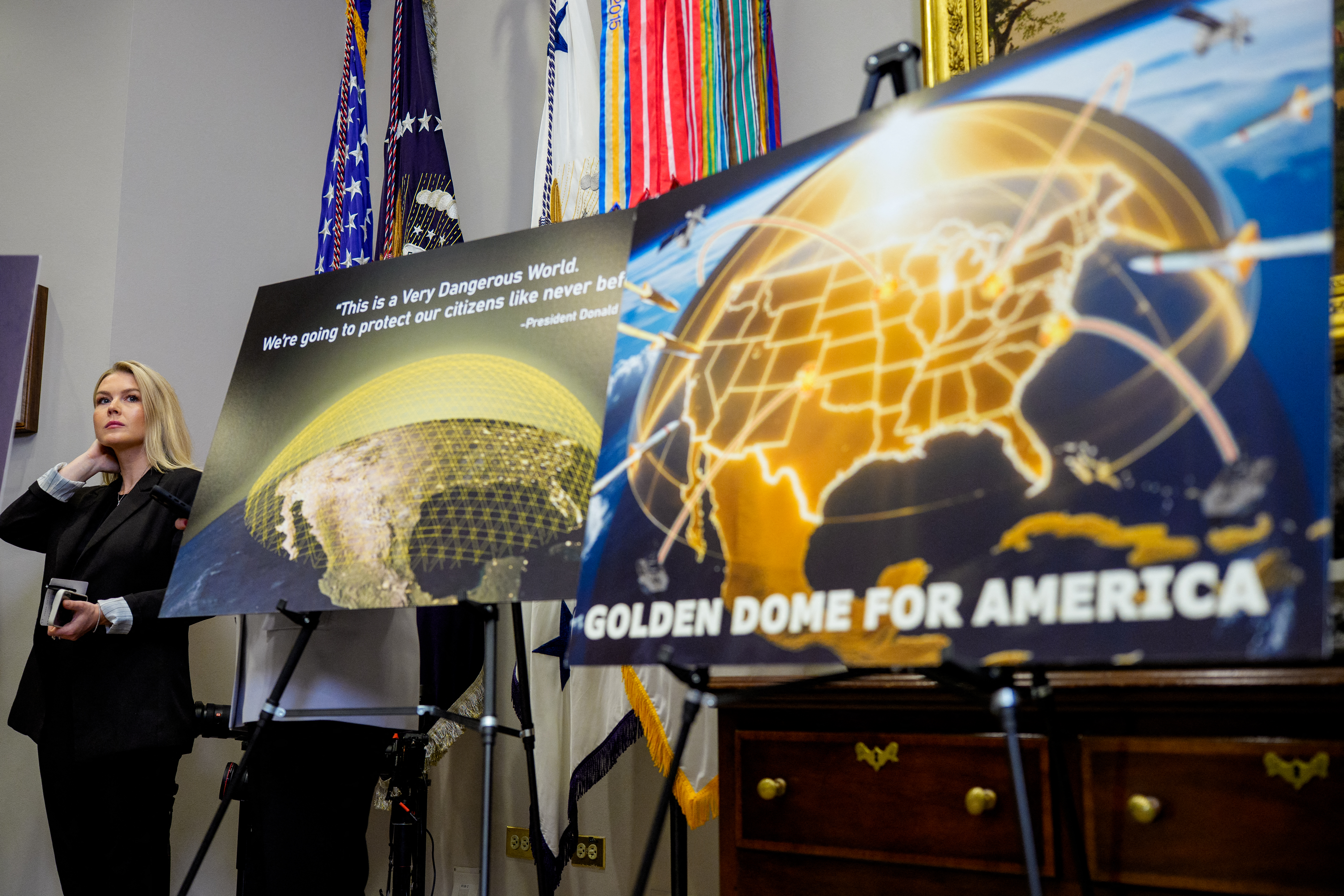 WASHINGTON, DC - MAY 12: White House press secretary Karoline Leavitt looks on from behind a chart on prescription drug costs and posters depicting a "Golden Dome for America" as U.S. President Donald Trump speaks during a press conference in the Roosevelt Room of the White House on May 12, 2025, in Washington, DC. During the event, President Trump signed an executive order aimed at reducing the cost of prescription drugs and pharmaceuticals by 30% to 80%. Andrew Harnik/Getty Images/AFP (Photo by Andrew Harnik / GETTY IMAGES NORTH AMERICA / Getty Images via AFP)