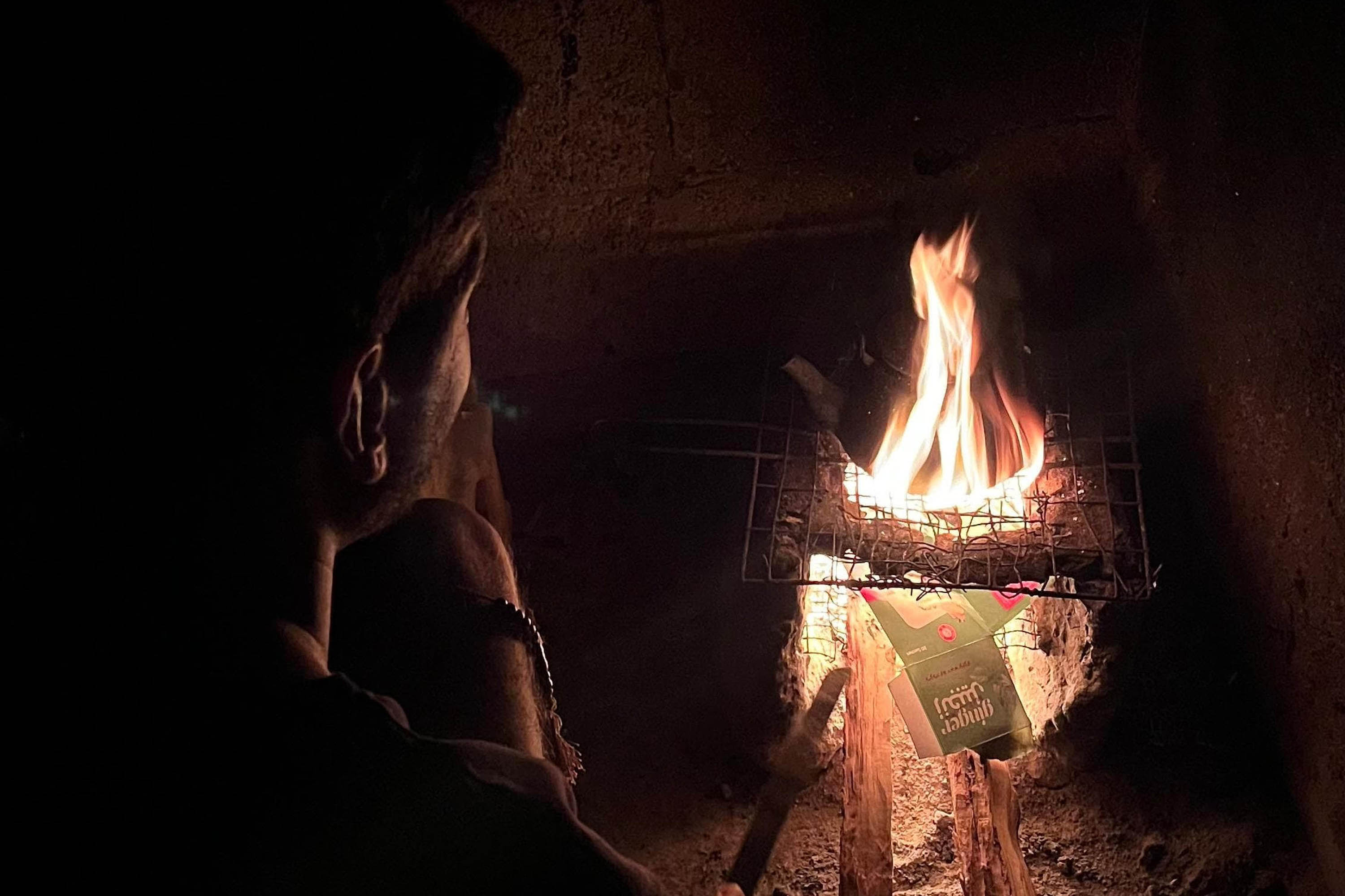 A photo of a man sitting close to fire on which a pot of water is boiling