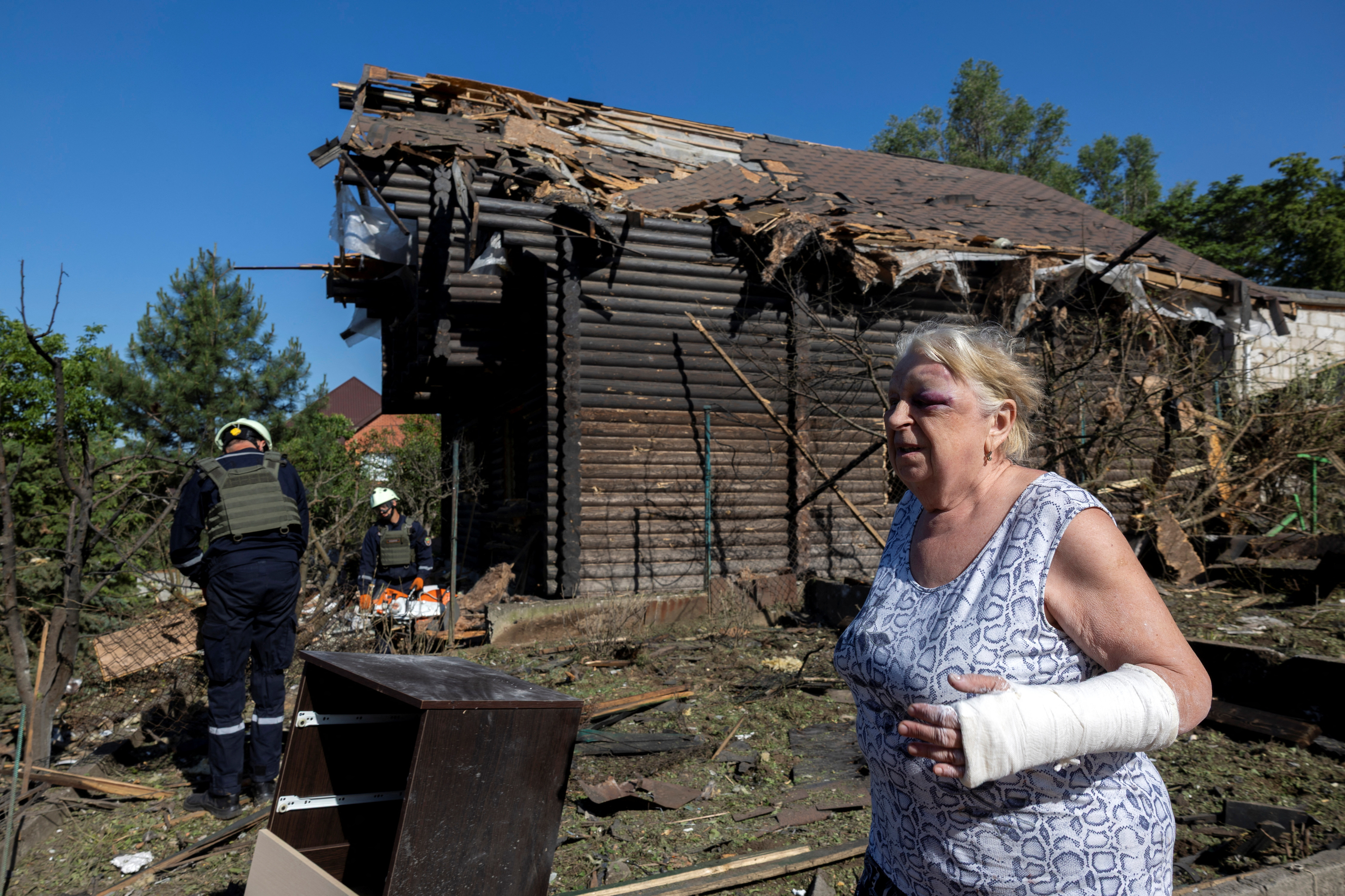 a woman with an injured arm in a cast stands in front of a damaged home