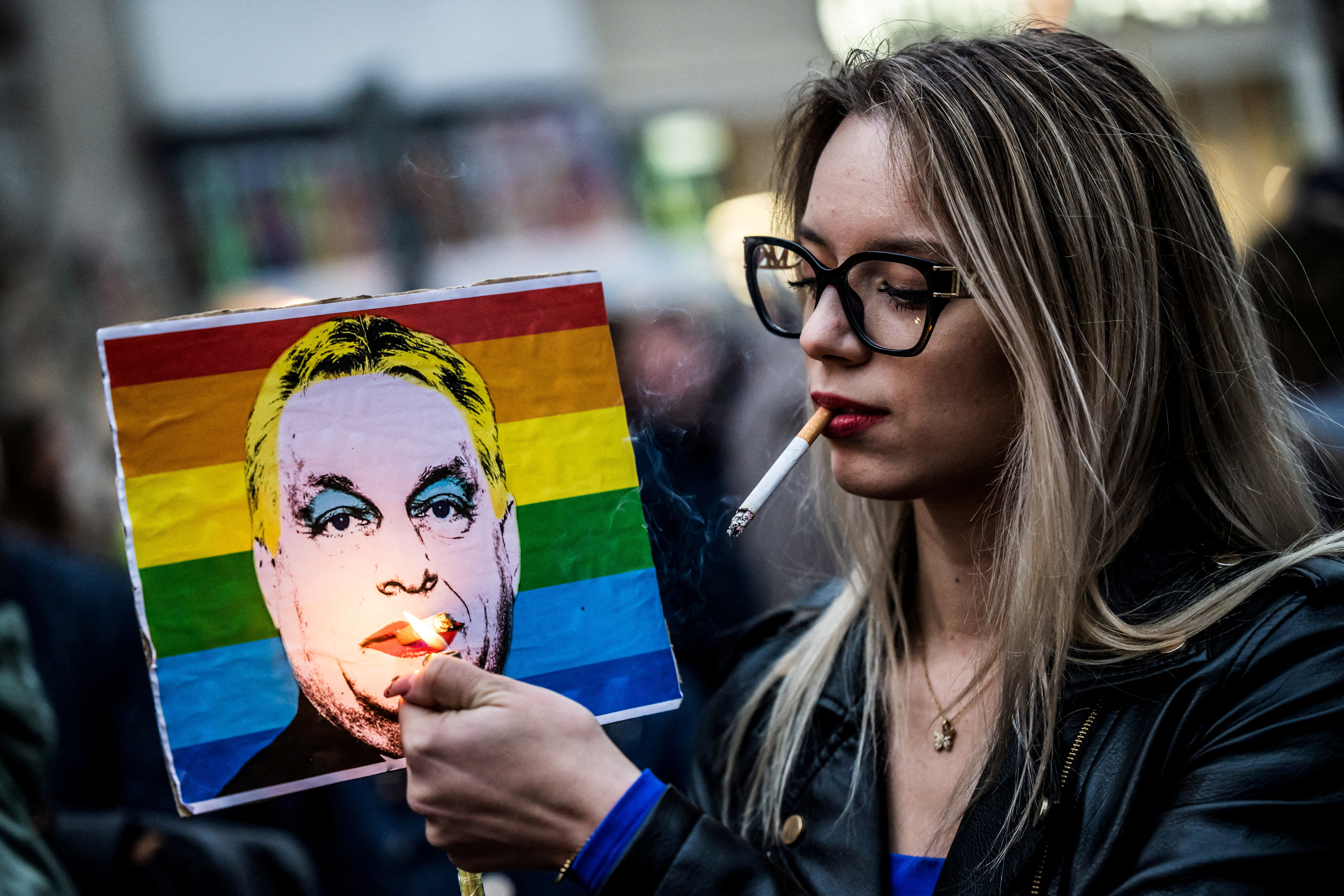 FILE PHOTO: A woman lights a cigarette placed in a placard depicting Hungary's Prime Minister Viktor Orban, during a demonstration, after the Hungarian parliament passed a law that bans LGBTQ+ communities from holding the annual Pride march and allows a broader constraint on freedom of assembly, in Budapest, Hungary, March 25, 2025. REUTERS/Marton Monus/File Photo