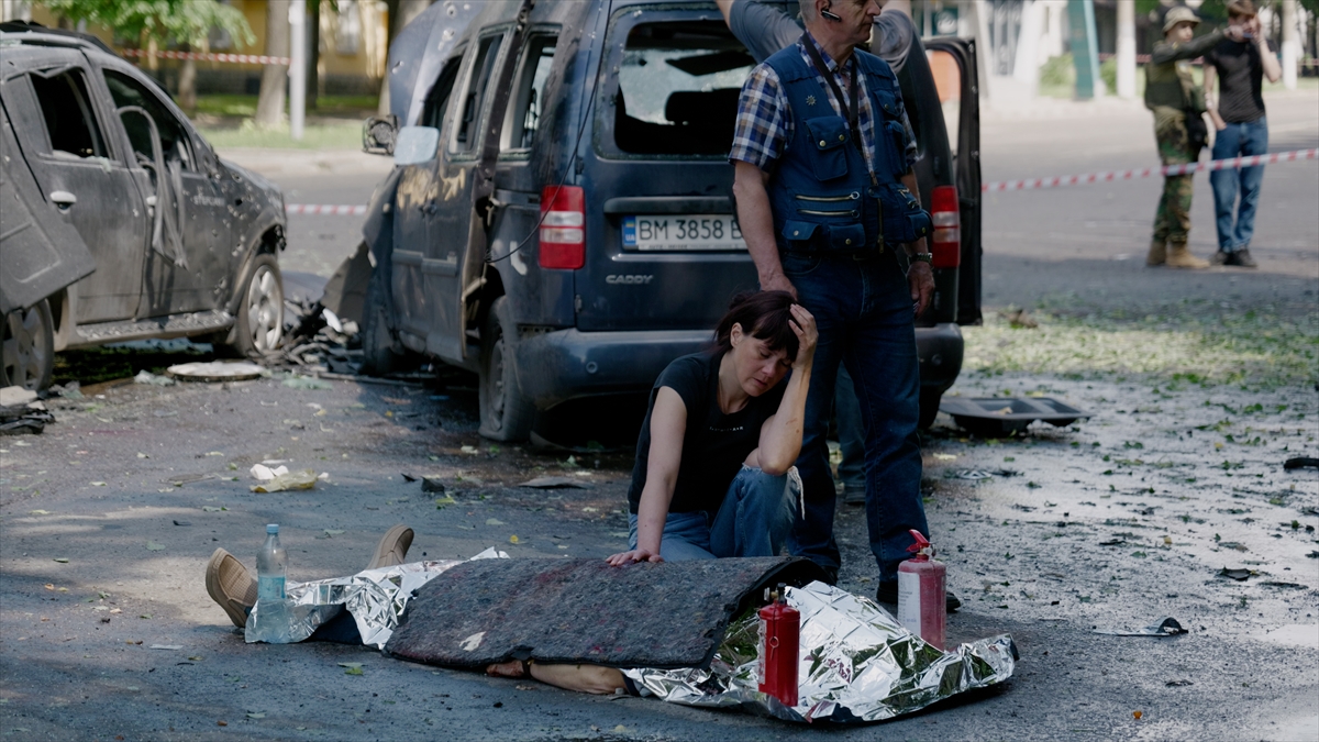 a woman kneels over a body covered in a foil blanket