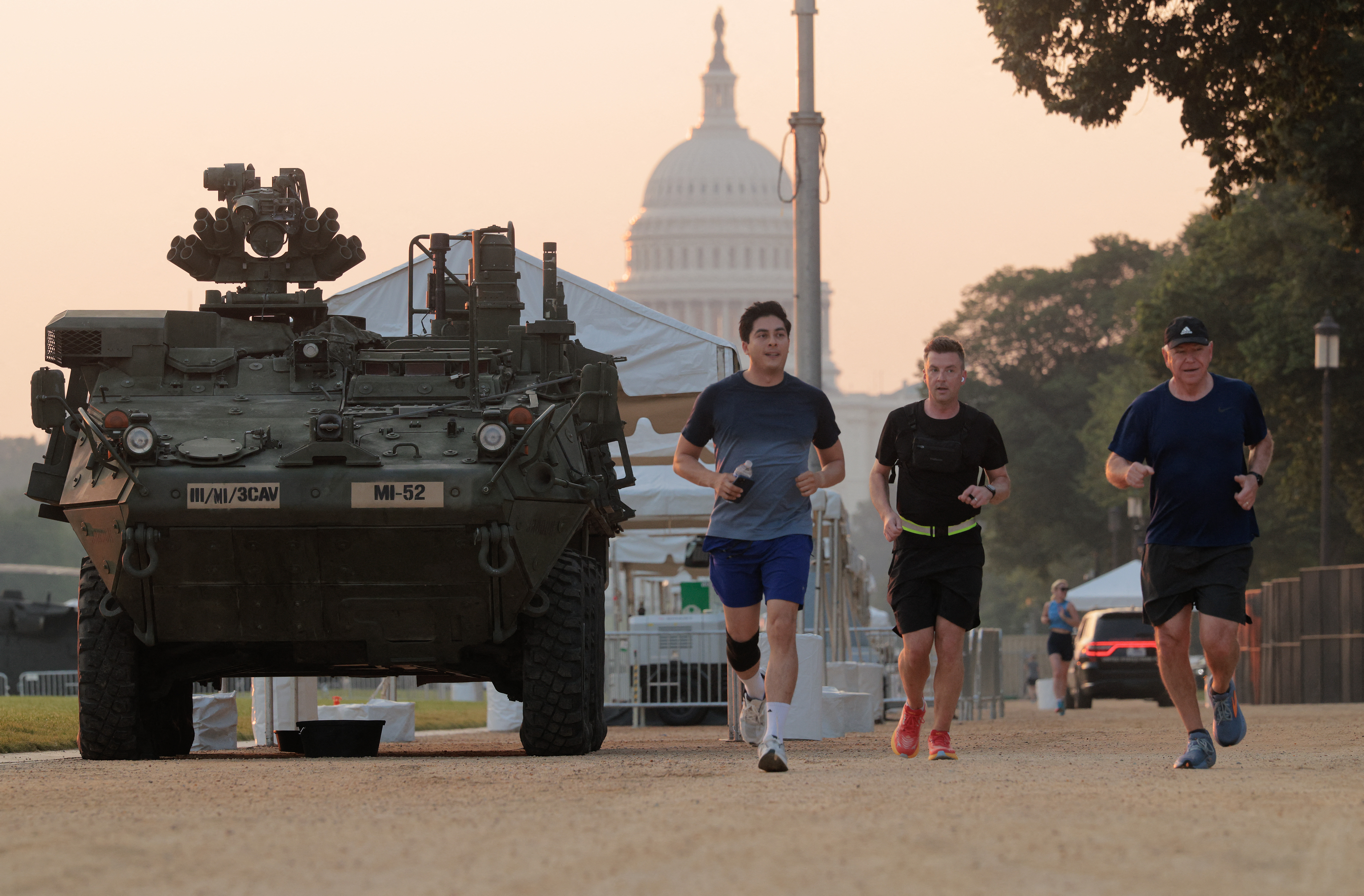 WASHINGTON, DC - JUNE 12: Minnesota Gov. Tim Walz (R) runs past a U.S. Army Stryker combat vehicle at dawn along the National Mall ahead of this weekend's military parade and celebration on June 12, 2025 in Washington, DC. The Army will mark its 250th anniversary Saturday, which is also President Donald Trump's birthday, with a parade along the National Mall that will include 6,500 troops, 150 vehicles and 50 aircraft, which will cost between $25 million and $45 million. Chip Somodevilla/Getty Images/AFP (Photo by CHIP SOMODEVILLA / GETTY IMAGES NORTH AMERICA / Getty Images via AFP)