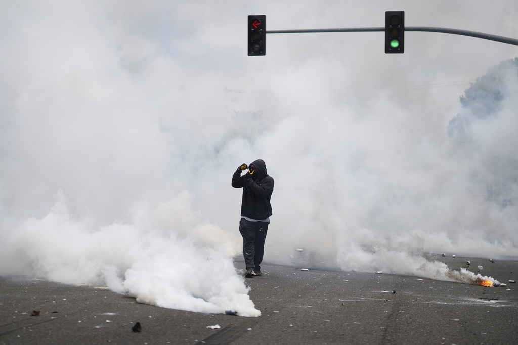 a person wearing black walks through tear gas smoke