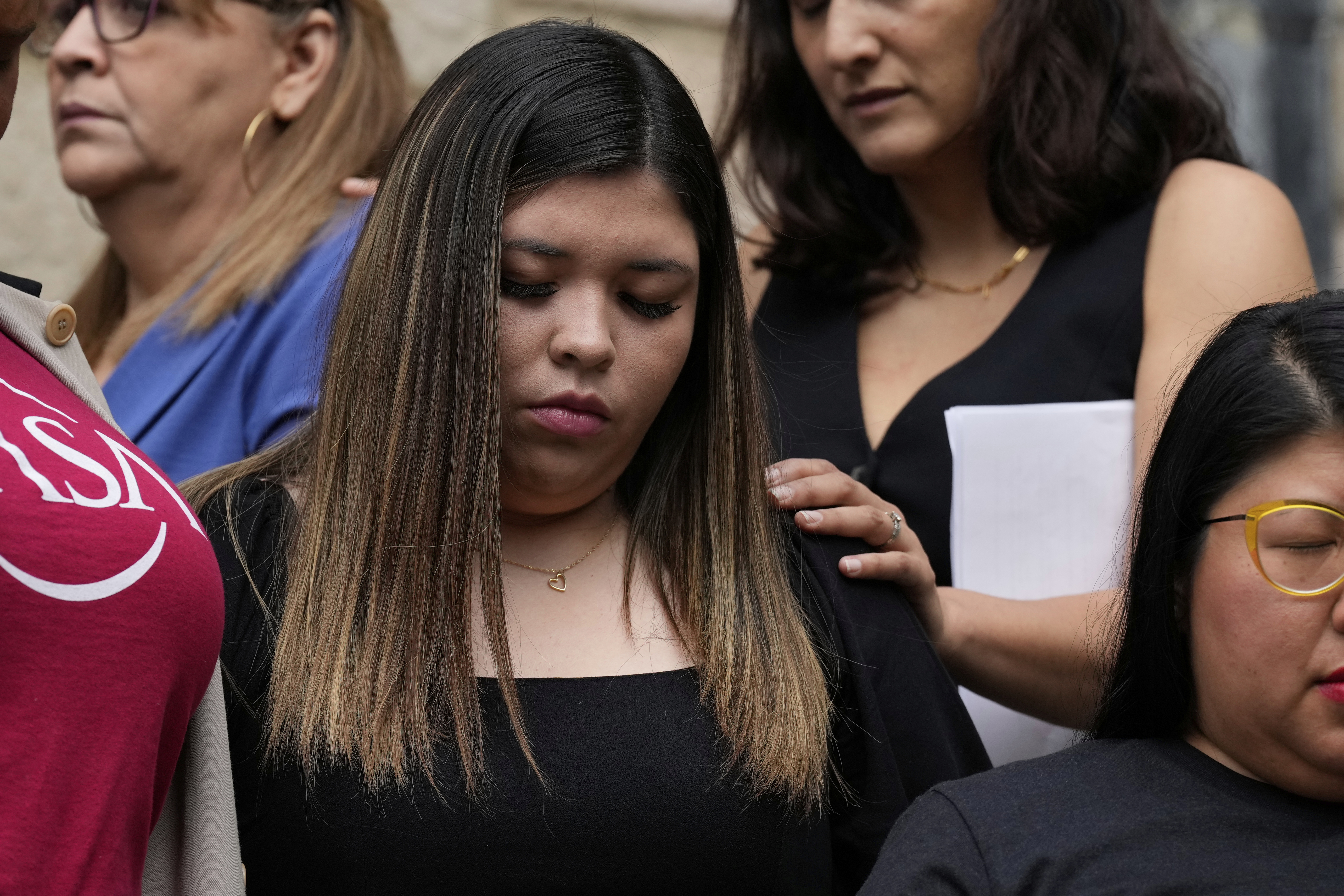 Jennifer Vasquez Sura stands at a press conference, with someone pressing a hand on her shoulder in comfort.