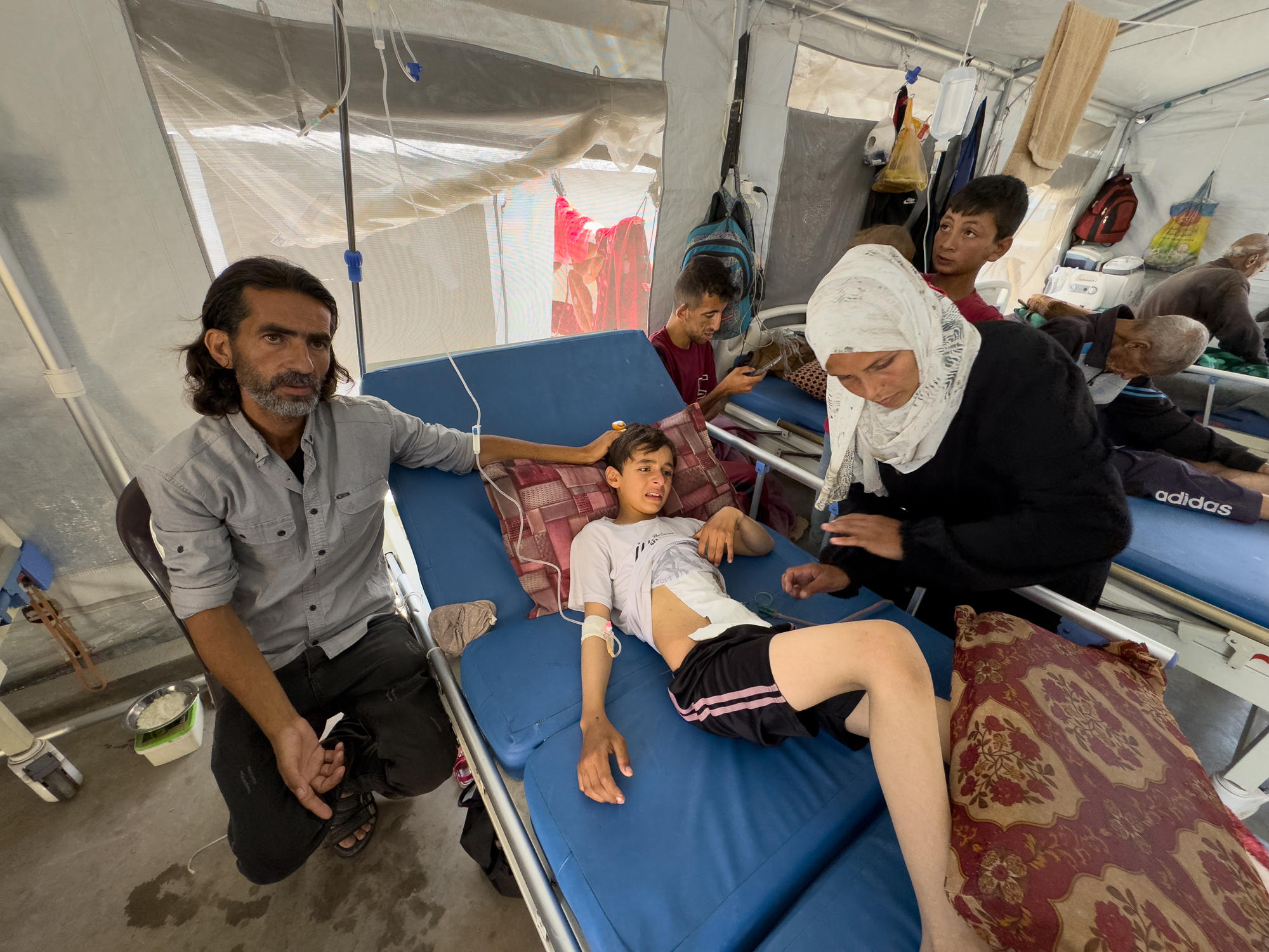 Ihab and Iman Musleh hover near their son's hospital bed in a makeshift tent ward