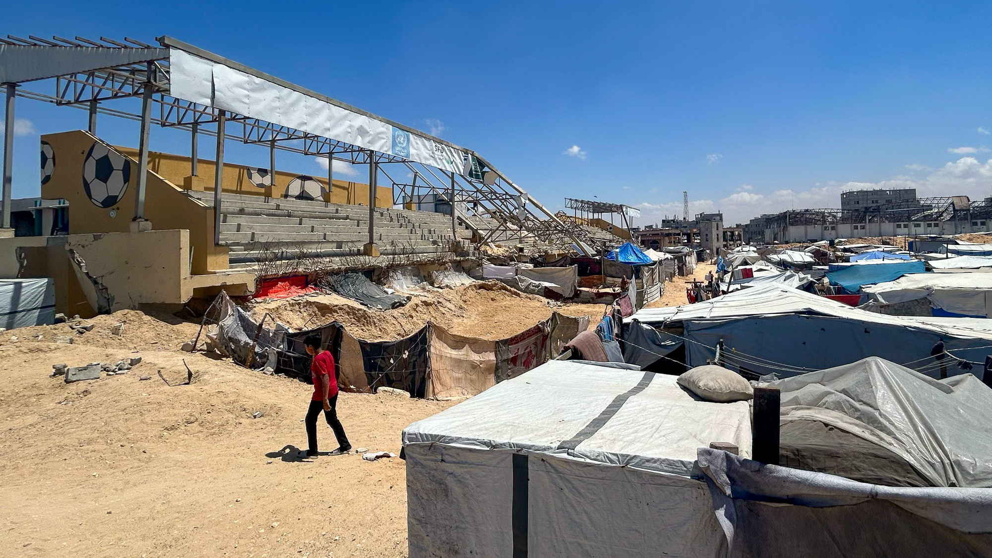 Partially-destroyed Khan Younis football stadium with shelters beside the grandstand.