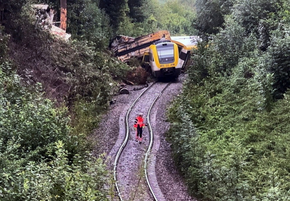 a person wearing orange walks along train tracks in front of a derailed train