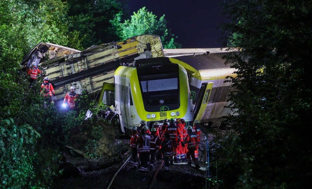 a view of train carriages piled on top of each other at night while people in red uniforms walk past