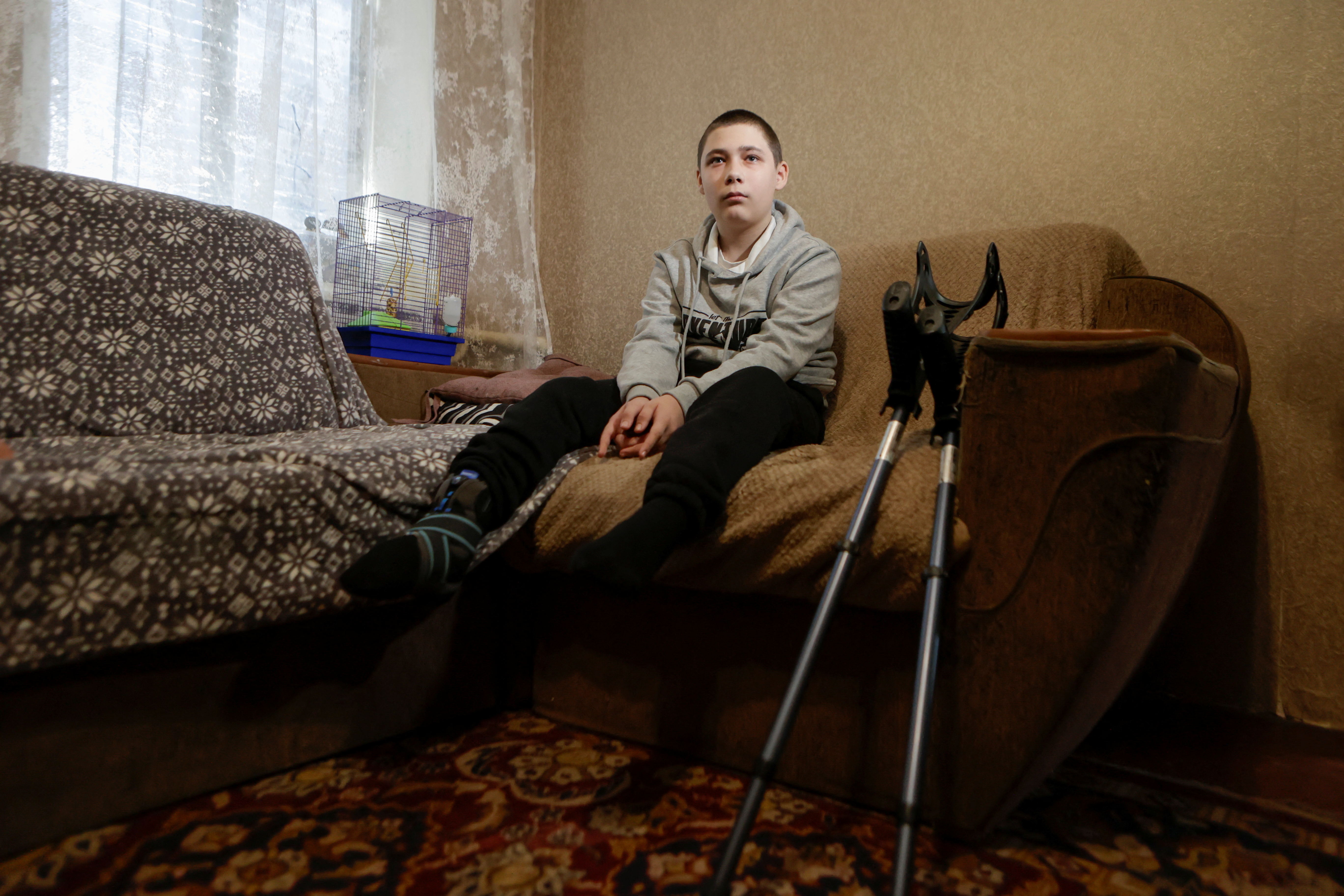 Nazar Mostovyi, 13-year-old, who was injured when an explosive device blew up under his feet, sits on a sofa inside of his house, amid Russia's attack on Ukraine, in the village of Nikopol, Kharkiv region, Ukraine May 13, 2025. REUTERS/Sofiia Gatilova