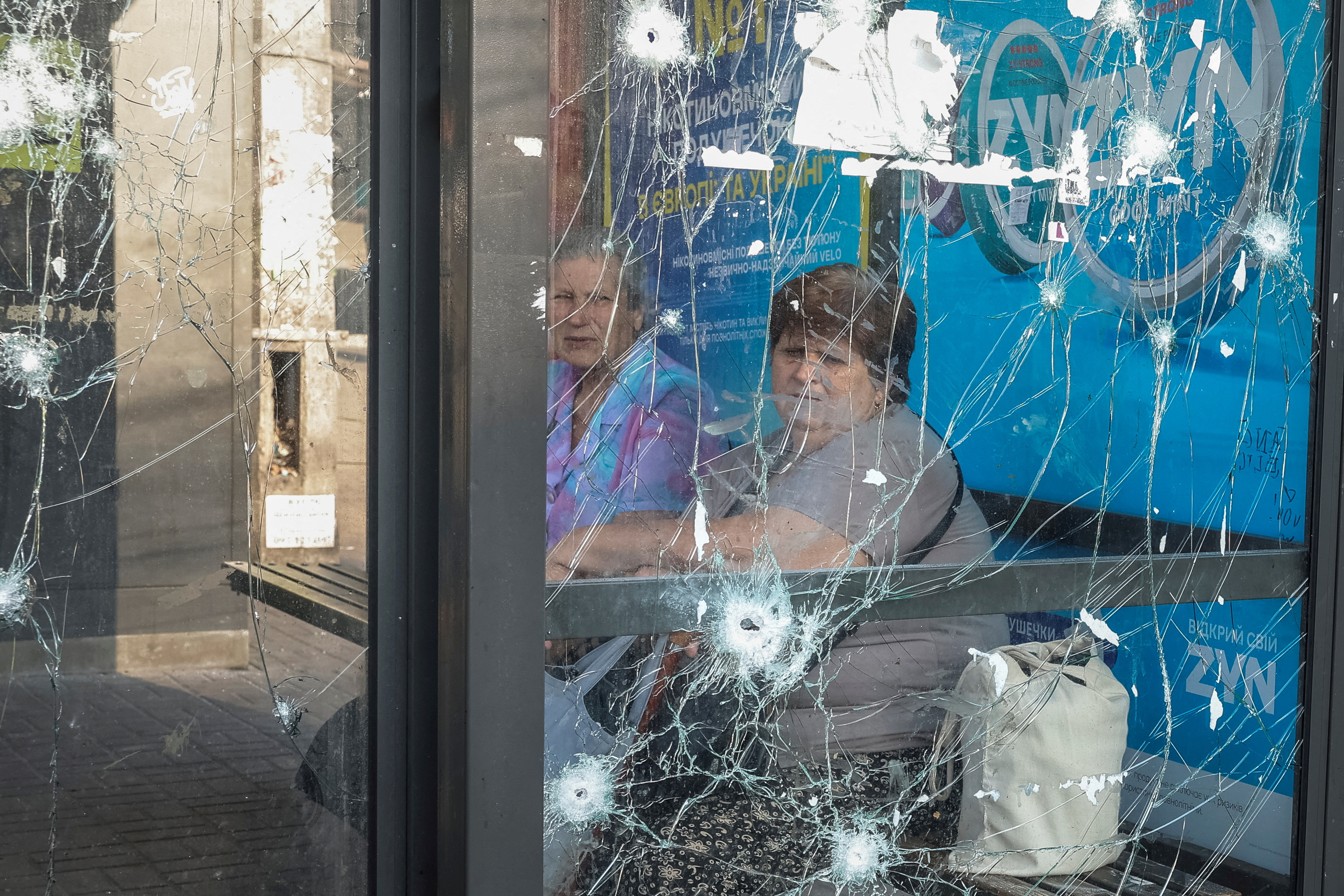 Women sit at a bus stop damaged during Russian drone and missile strikes, amid Russia’s attack on Ukraine, in Kyiv, Ukraine July 10, 2025. REUTERS/Alina Smutko TPX IMAGES OF THE DAY