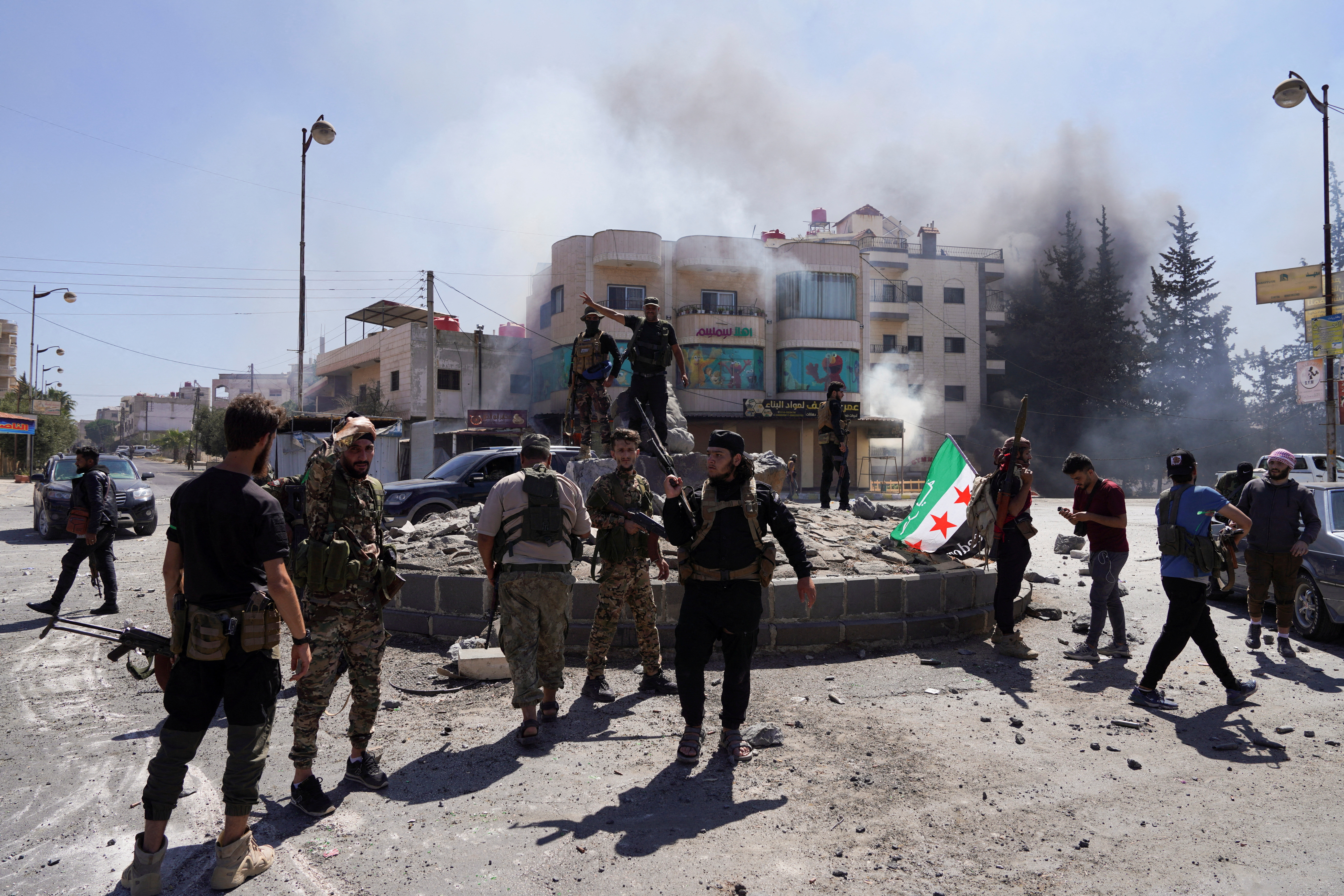 smoke rises in the distances as soldiers hold a Syrian flag