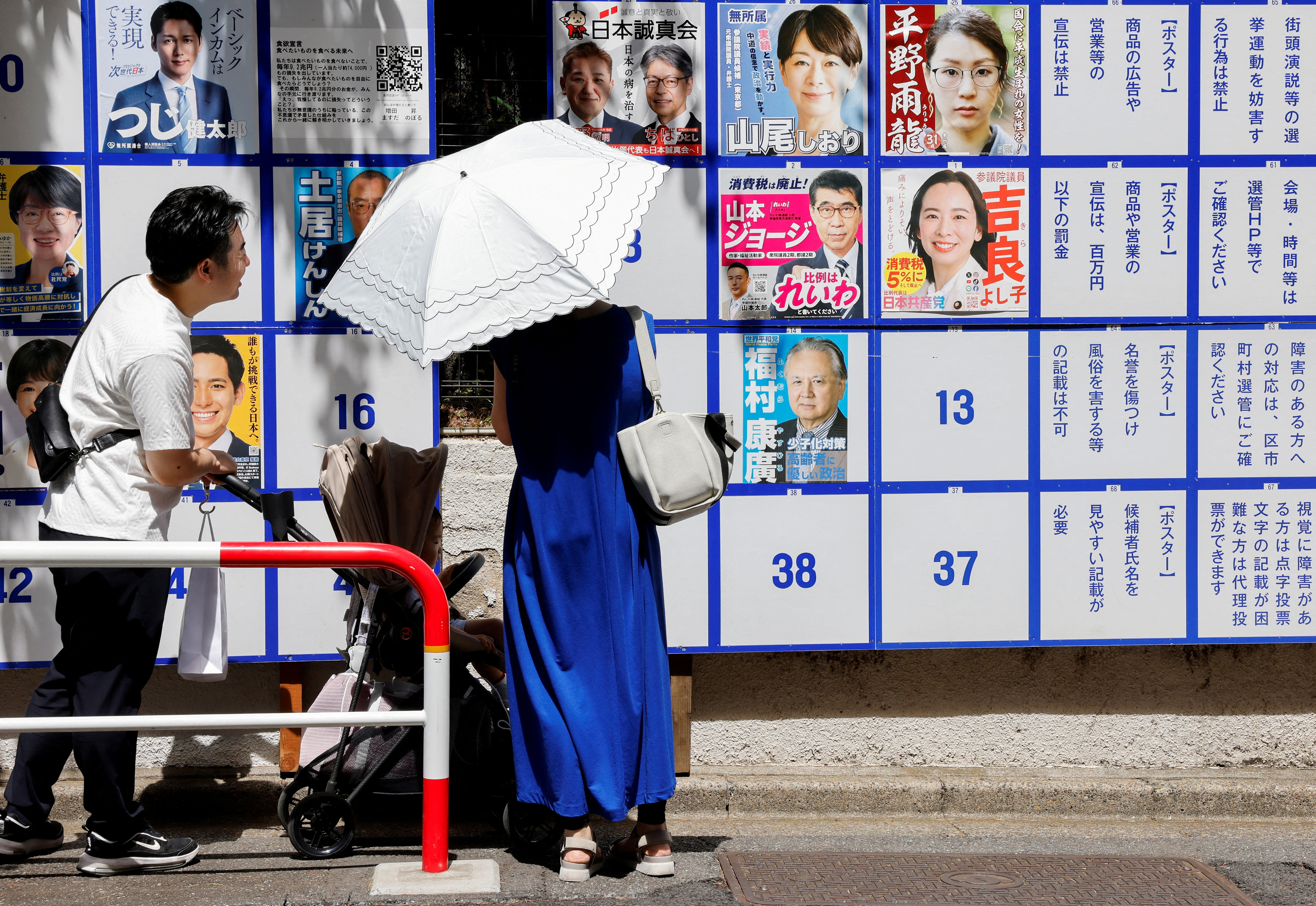 a woman with a white umbrella looks at brightly coloured posters on a wall