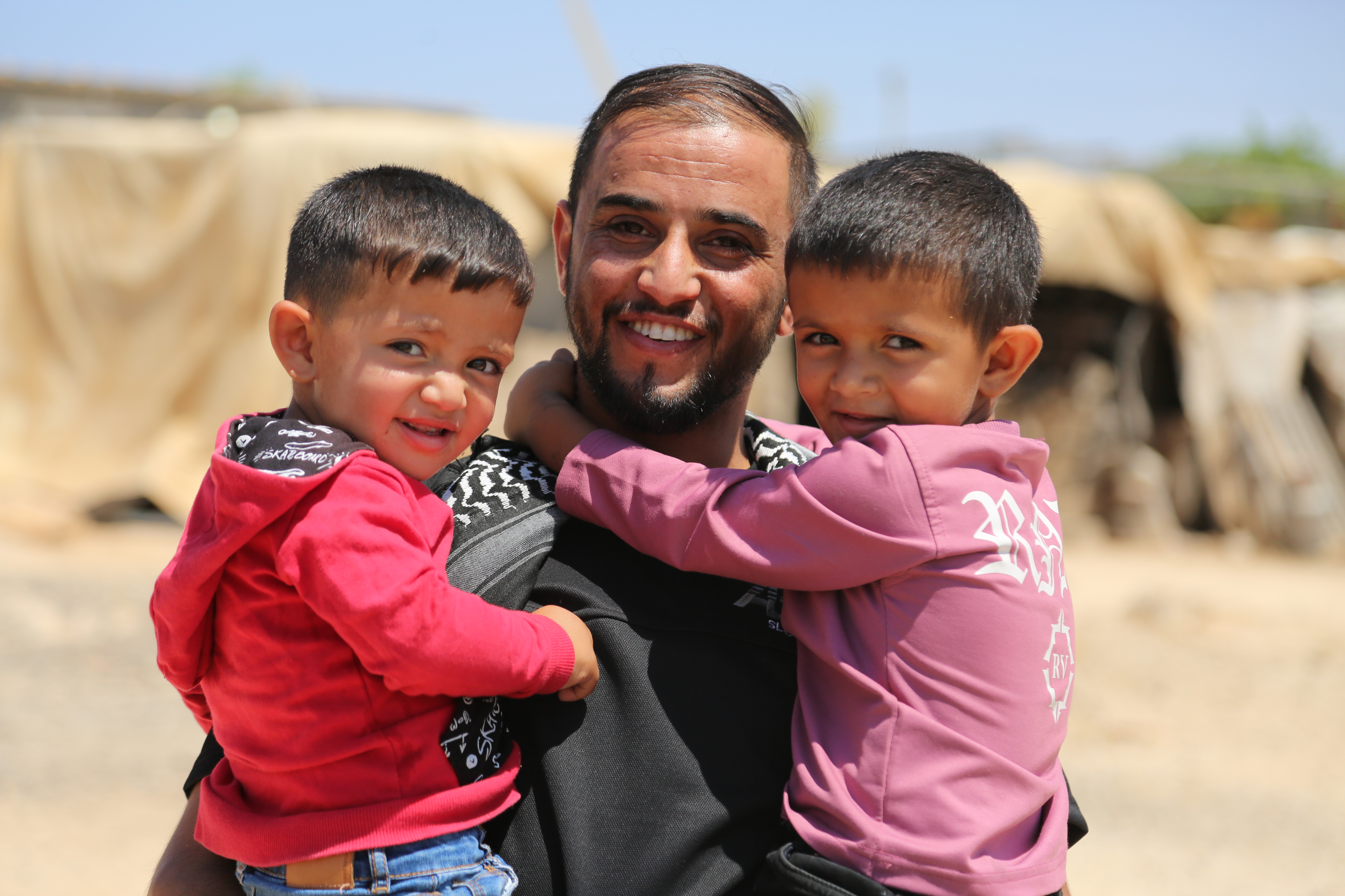 Two cute boys cling to their uncle's neck and look at the camera.