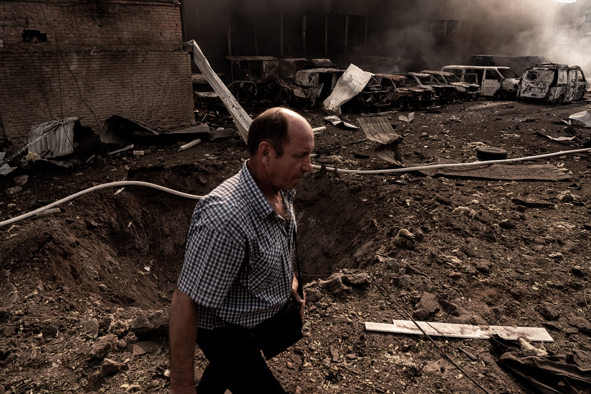 a man walks past a hole in the ground next to burnt out cars