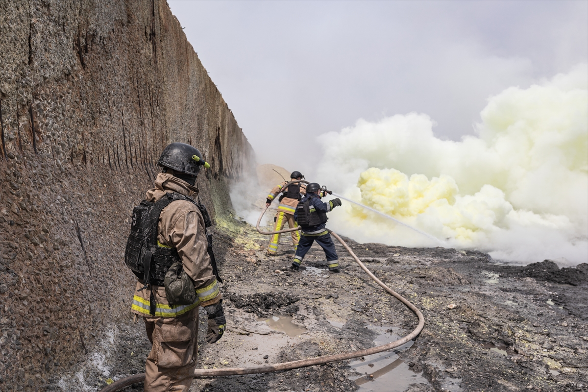 firefighters spray water on a yellow rising cloud of smoke