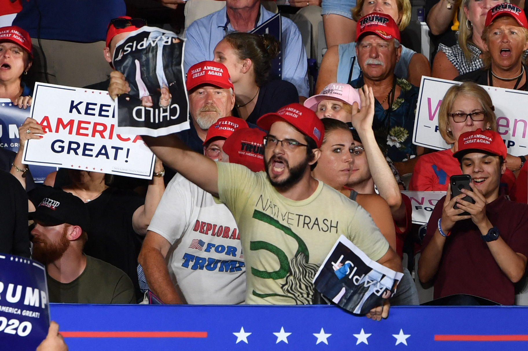 A protester holds a photo of US President Donald Trump with Jeffrey Epstein, the financier accused of sexually abusing young girls, and reading "child rapist" during a "Make America Great Again" rally at Minges Coliseum in Greenville, North Carolina, on July 17, 2019. (Photo by Nicholas Kamm / AFP)