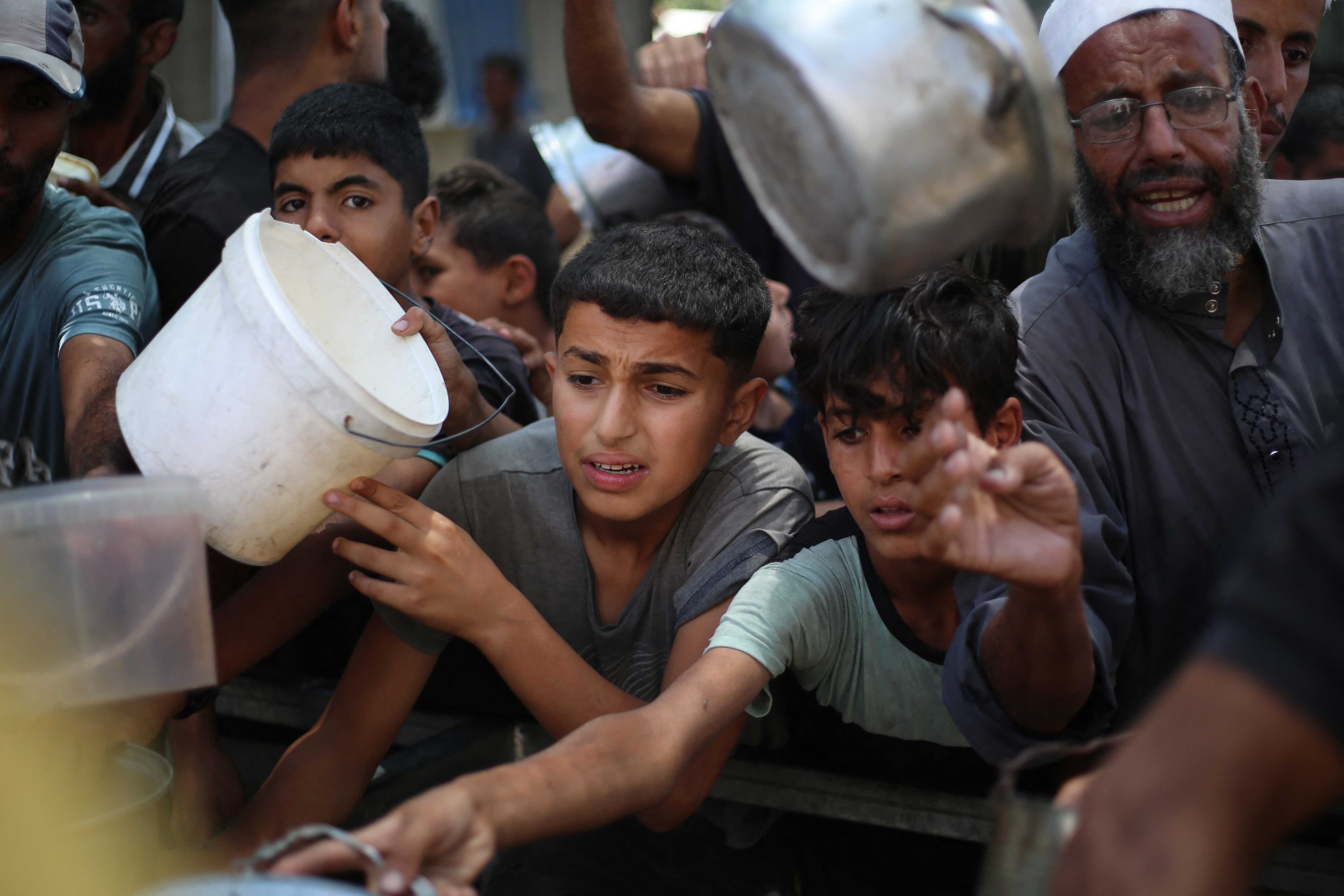 Palestinian children queue for a portion of hot food distributed by a charity kitchen at the Nuseirat refugee camp. The UN aid agency for Palestinian refugees (UNRWA) aid Tuesday that one in 10 children screened in their facilities are now malnourished. [Eyad Baba/AFP]