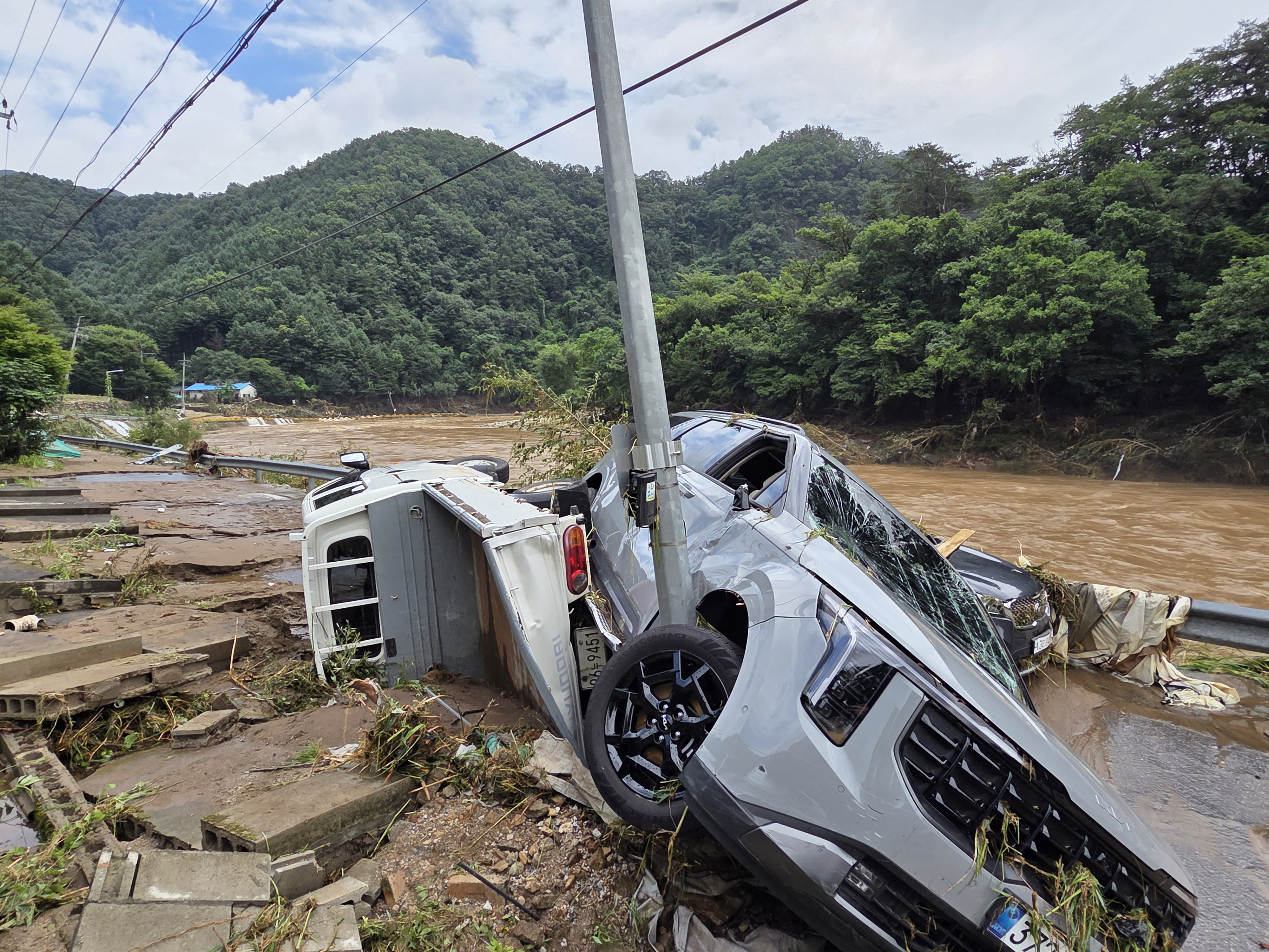 TOPSHOT - Cars damaged by floodwater are seen on a road along the river due to heavy rain in Gapyeong county on July 20, 2025. At least two people were killed during heavy downpours early on July 20, the interior ministry said, bringing the death toll to 14 as South Korea has been hit by torrential rainfall this week. (Photo by YONHAP / AFP) / NO USE AFTER AUGUST 19, 2025 15:00:00 GMT - - SOUTH KOREA OUT / NO ARCHIVES - RESTRICTED TO SUBSCRIPTION USE