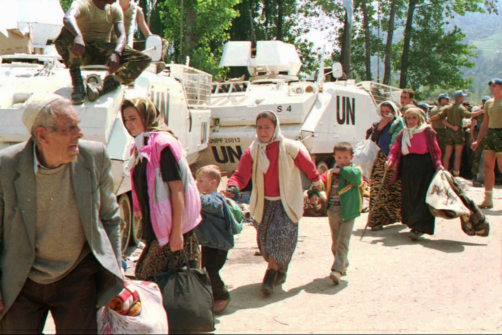 FILE - Muslim refugees from Srebrenica, eastern Bosnia, pass by UN armored personnel carriers.