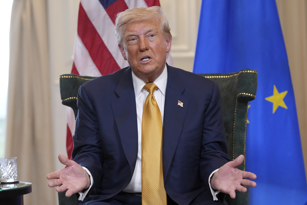 a man in a yellow tie sits in front of a US and EU flag