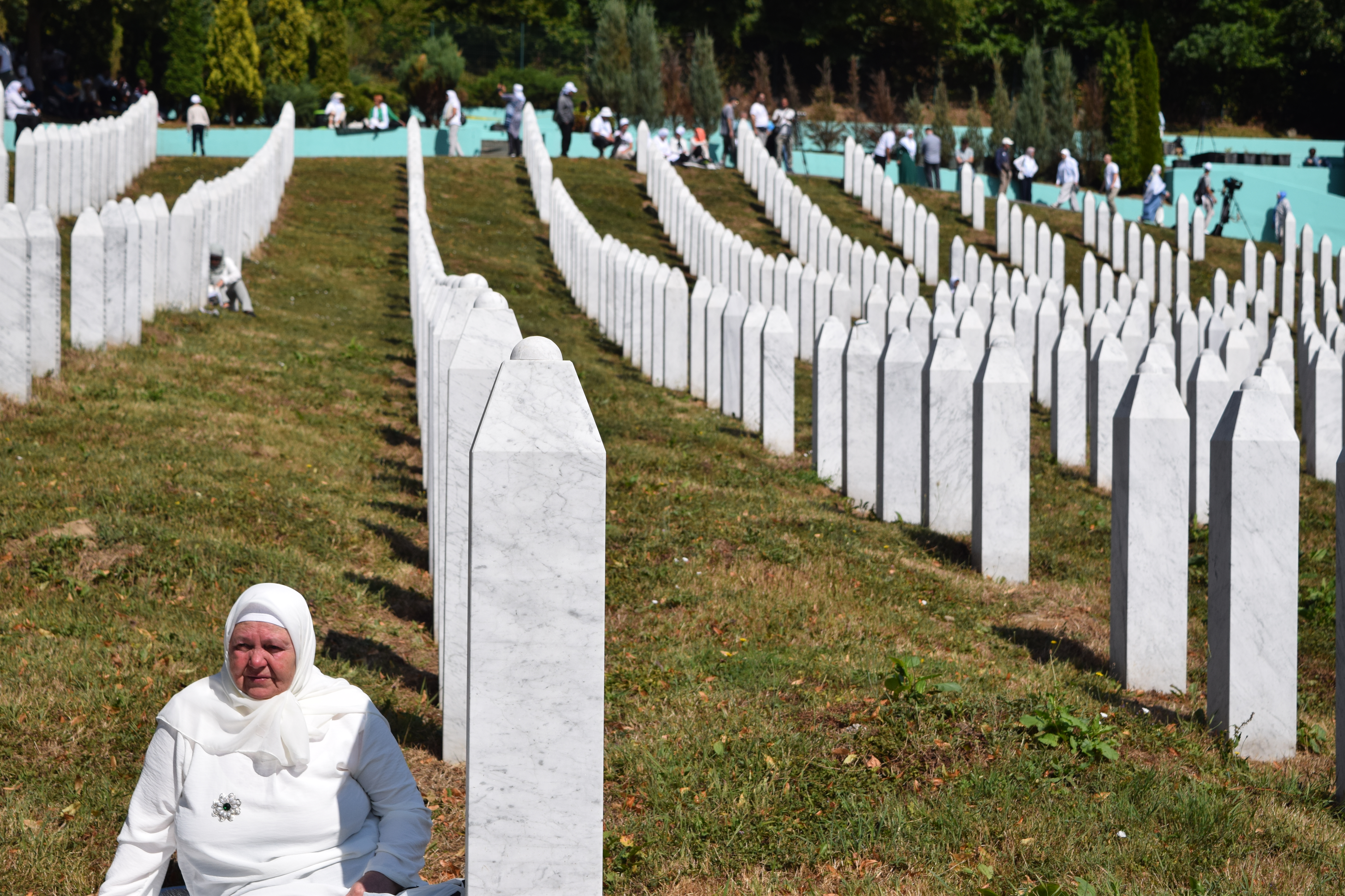A woman sits next to the gravestone of a relative at the Srebrenica Genocide Memorial in Potocari